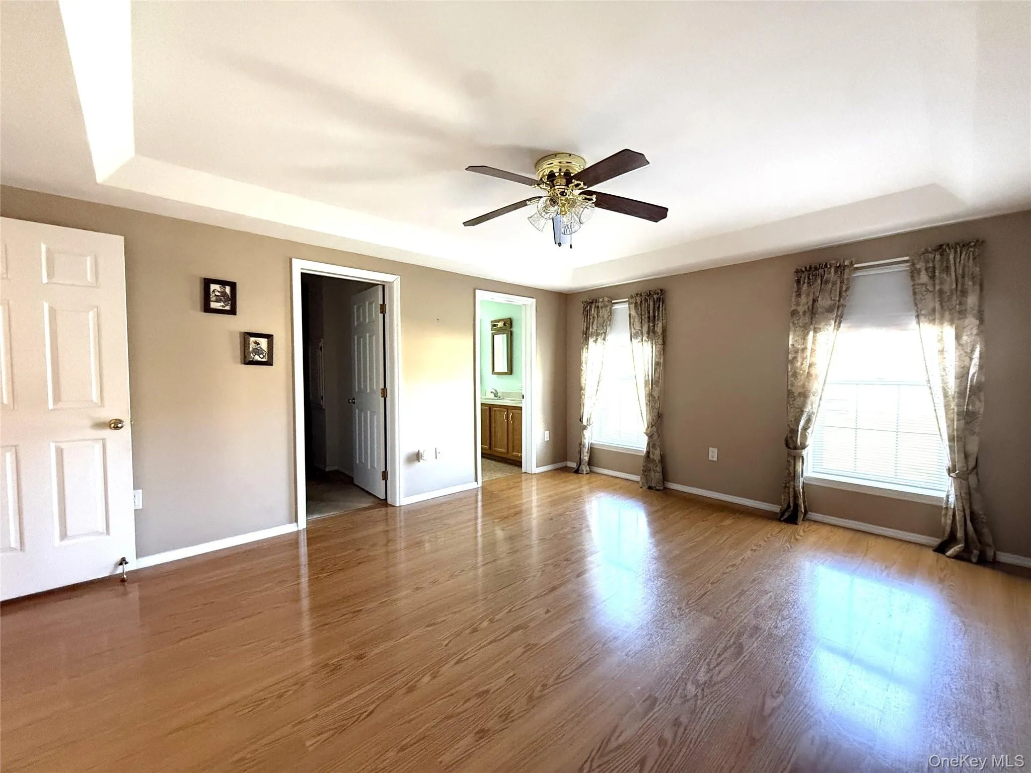 Tray ceiling, wood-finish flooring, and a multi-light ceiling fan and natural light. Tray ceiling, wood-finish flooring, and a multi-light ceiling fan and natural light.