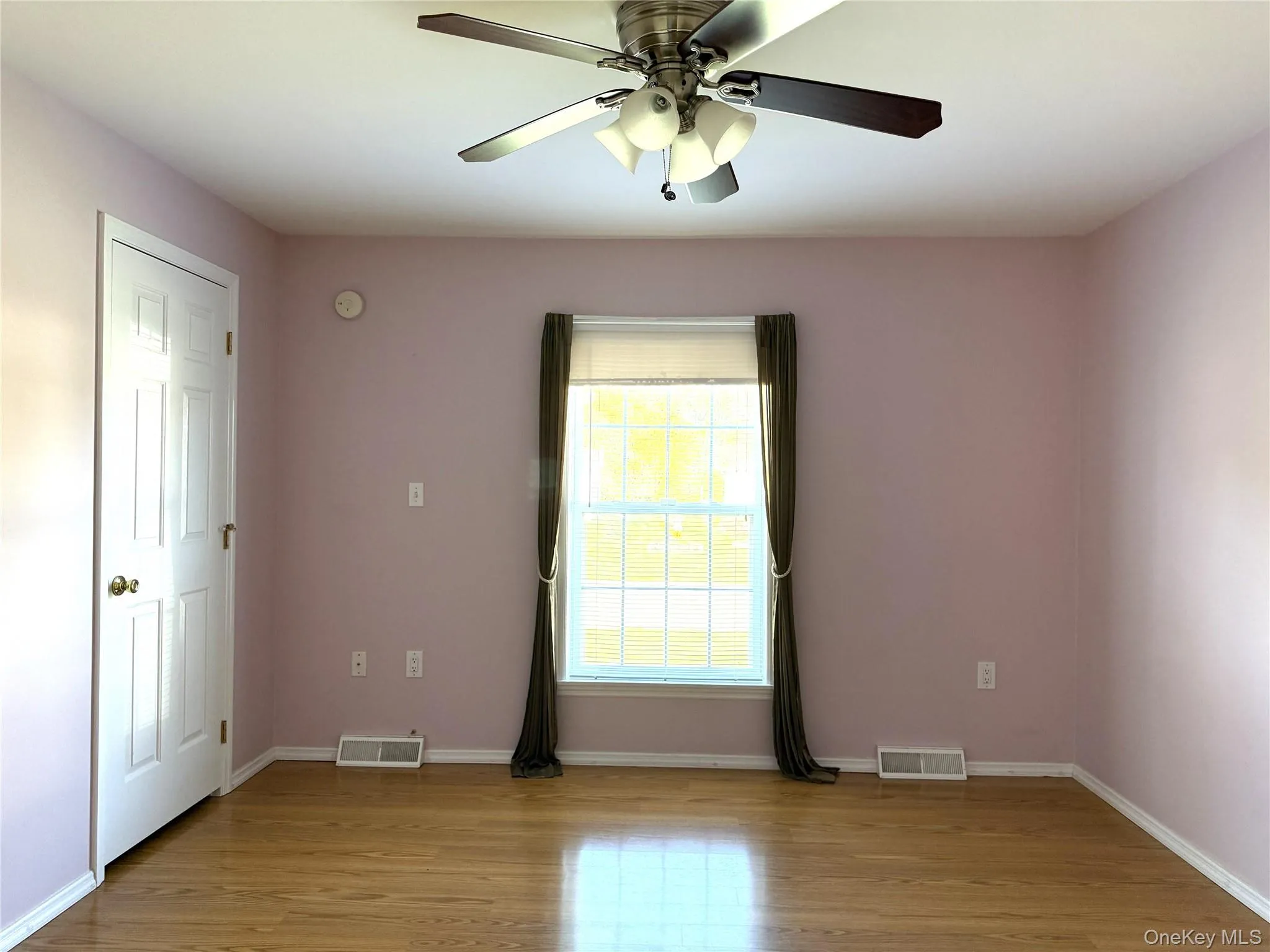 Room featuring wood-finish flooring, a multi-panel interior door, a central ceiling fan with integrated lighting, and a window with a multi-pane grid Room featuring wood-finish flooring, a multi-panel interior door, a central ceiling fan with integrated lighting, and a window with a multi-pane grid