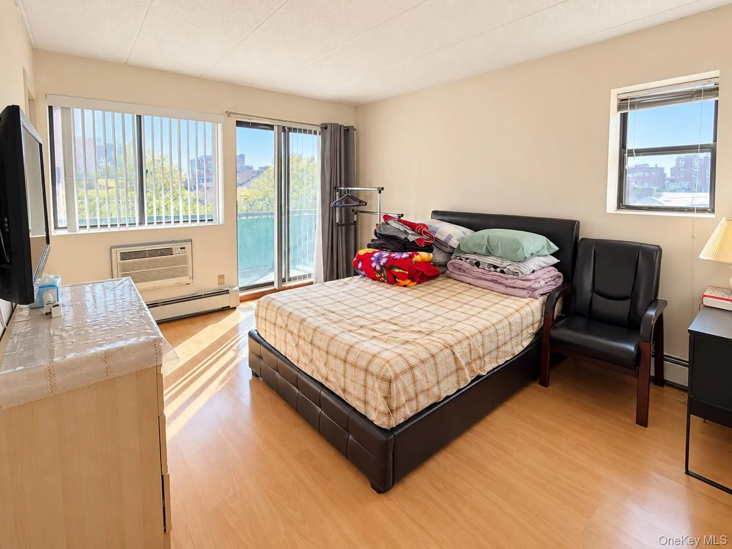 Wood-finish flooring, sliding glass door access to a balcony, large multi-pane windows, and a wall-mounted AC control unit Wood-finish flooring, sliding glass door access to a balcony, large multi-pane windows, and a wall-mounted AC control unit