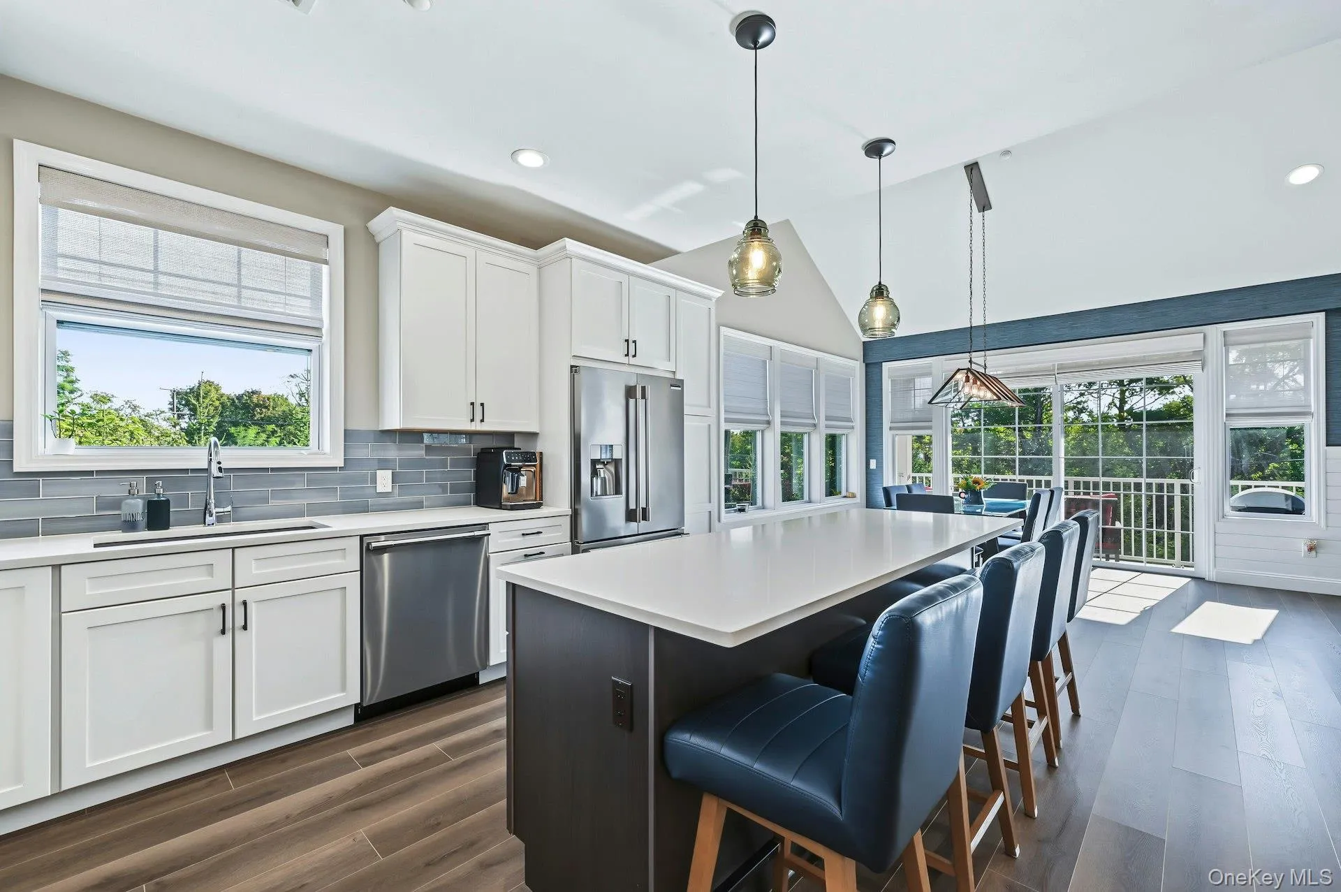 Kitchen featuring white cabinetry, center island with stone countertop, stainless steel appliances, wood-finish flooring, and vaulted ceilings with pendant lighting Kitchen featuring white cabinetry, center island with stone countertop, stainless steel appliances, wood-finish flooring, and vaulted ceilings with pendant lighting