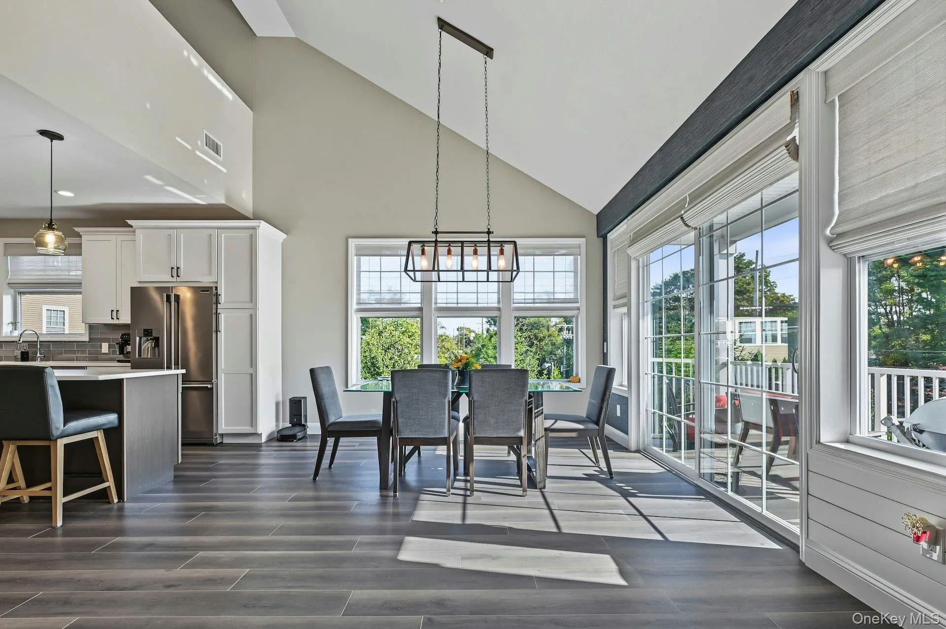 Vaulted ceilings, wood-finish plank flooring, large grid-pattern windows, multi-pane sliding glass doors, and a linear multi-light pendant fixture Vaulted ceilings, wood-finish plank flooring, large grid-pattern windows, multi-pane sliding glass doors, and a linear multi-light pendant fixture