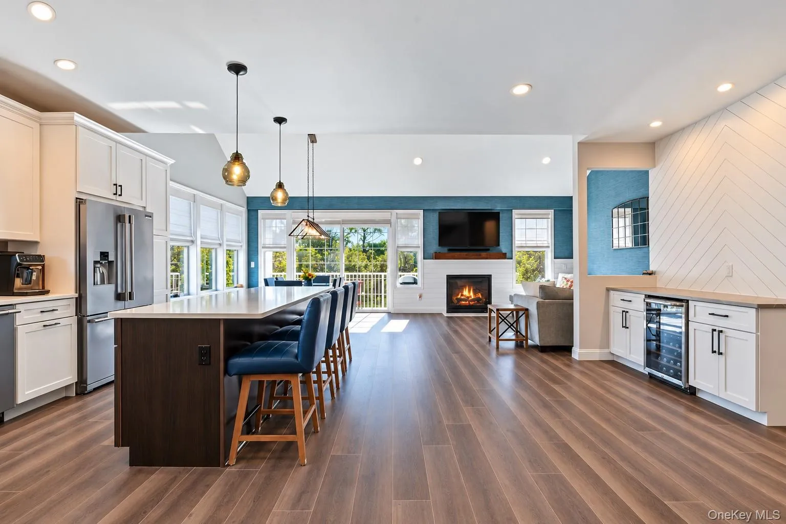 Kitchen featuring an island with a contrasting dark base, wood-finish flooring, a built-in beverage refrigerator, a gas fireplace with a wood mante Kitchen featuring an island with a contrasting dark base, wood-finish flooring, a built-in beverage refrigerator, a gas fireplace with a wood mante