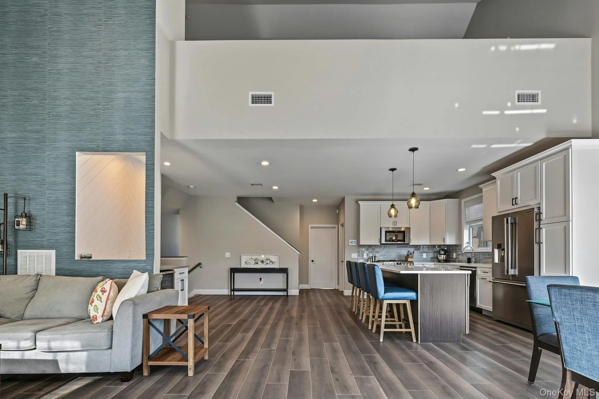 Vaulted ceilings with mezzanine level, blue textured accent wall featuring a recessed niche, kitchen island with stone-surface countertop, pendant lighting, and wood-finish flooring Vaulted ceilings with mezzanine level, blue textured accent wall featuring a recessed niche, kitchen island with stone-surface countertop, pendant lighting, and wood-finish flooring