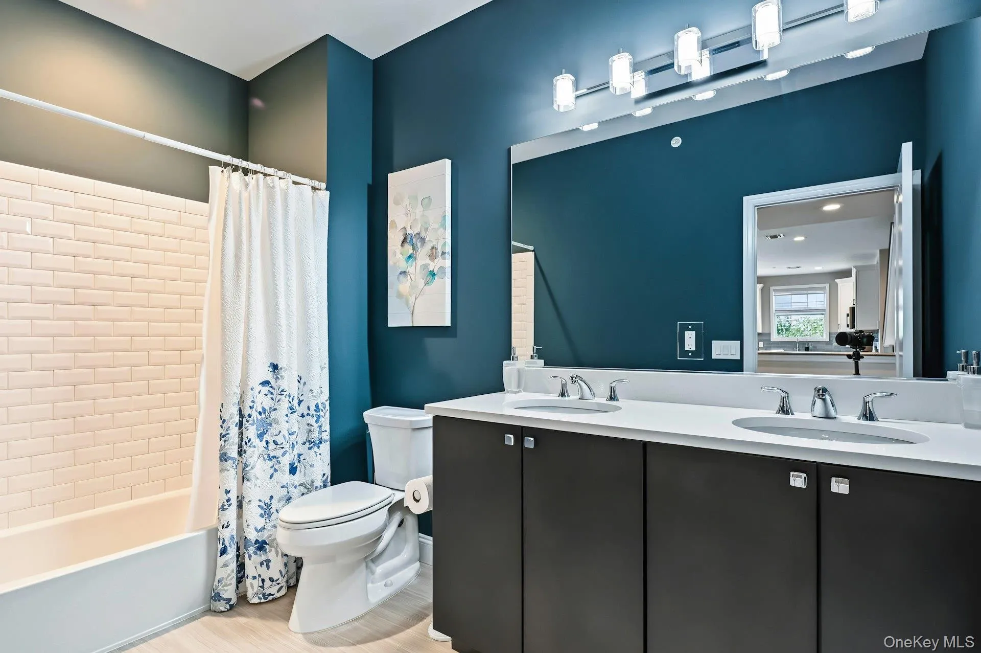 Double-vanity cabinet with stone-finish countertop, undermount sinks, mirror, subway-tile tub surround, and multi-bulb integrated vanity lighting Double-vanity cabinet with stone-finish countertop, undermount sinks, mirror, subway-tile tub surround, and multi-bulb integrated vanity lighting