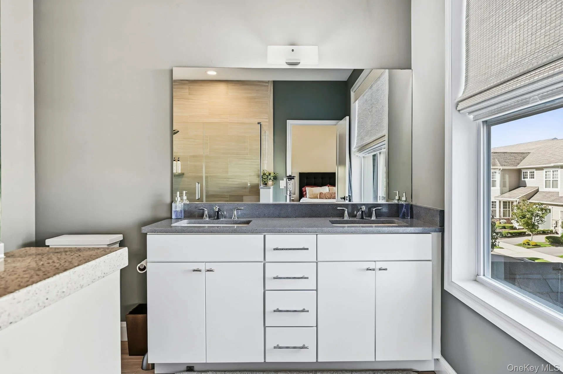Dual-sink vanity featuring a stone countertop, white cabinetry, polished chrome fixtures, and a window Dual-sink vanity featuring a stone countertop, white cabinetry, polished chrome fixtures, and a window