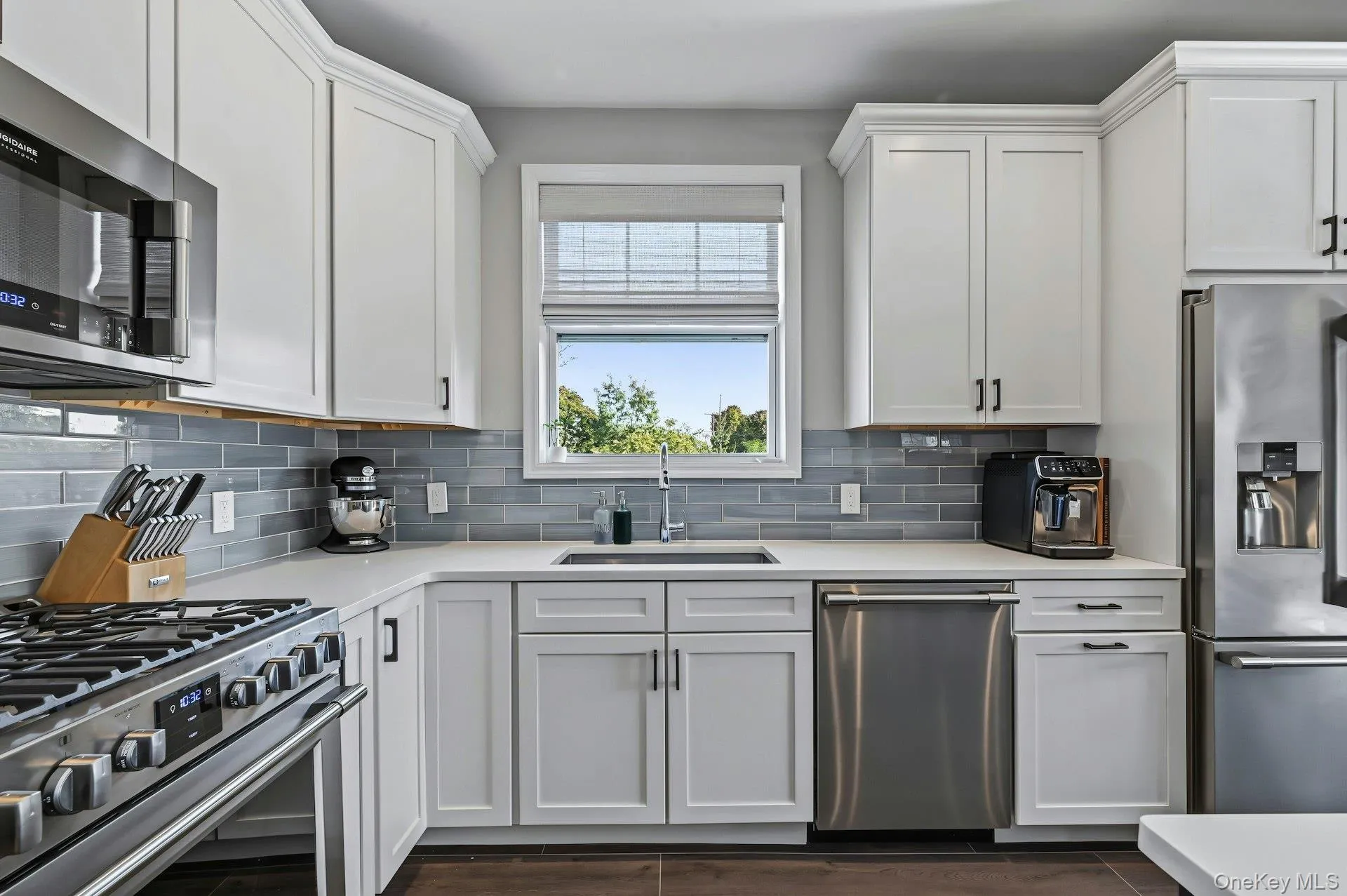 Kitchen featuring white shaker-style cabinetry, stainless steel appliances, quartz countertops, a grey subway tile backsplash, and a stainless steel sink Kitchen featuring white shaker-style cabinetry, stainless steel appliances, quartz countertops, a grey subway tile backsplash, and a stainless steel sink