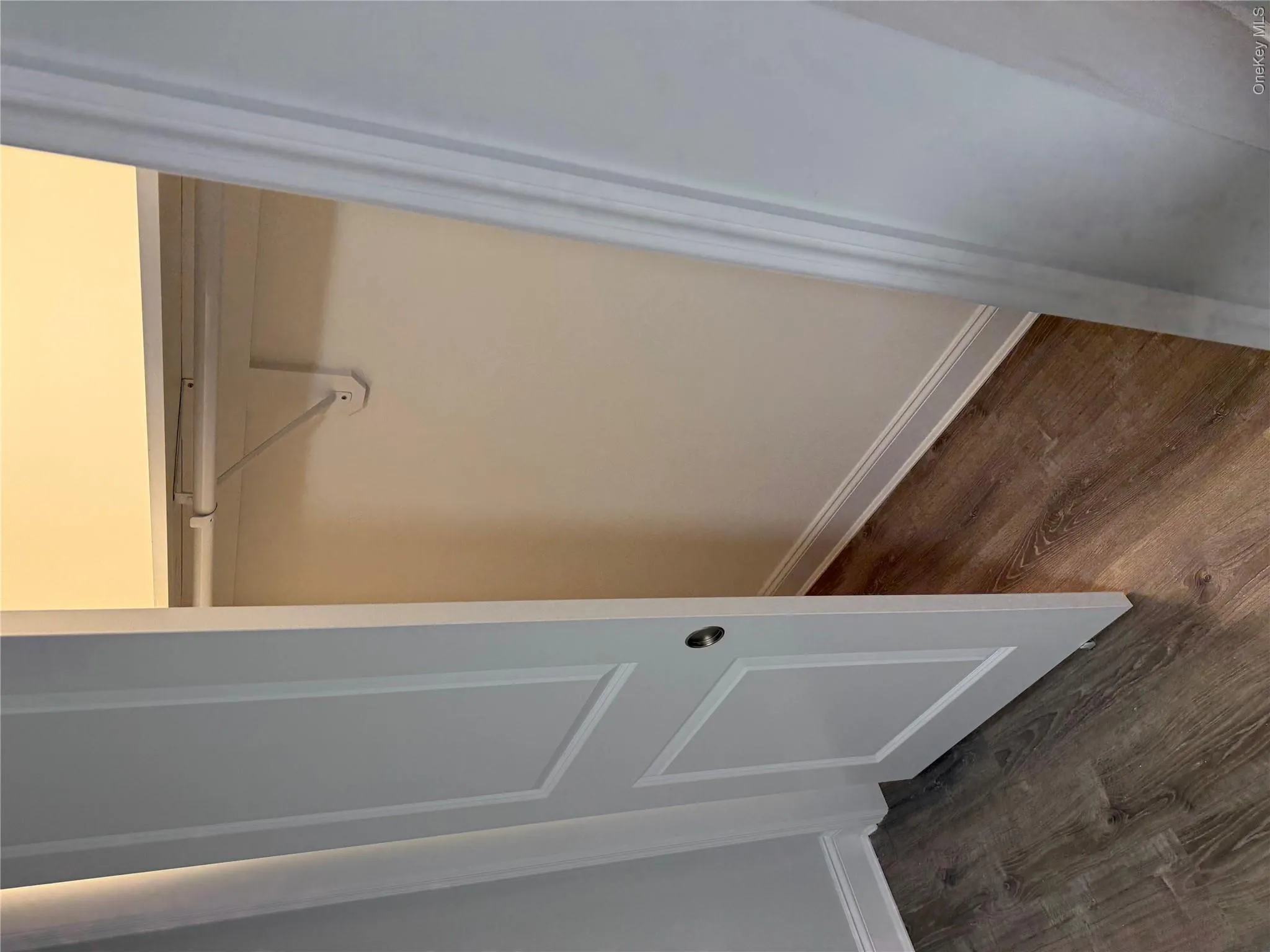 Storage closet featuring a two-panel interior door, wood-finish flooring, and a built-in shelf with a clothing rod Storage closet featuring a two-panel interior door, wood-finish flooring, and a built-in shelf with a clothing rod