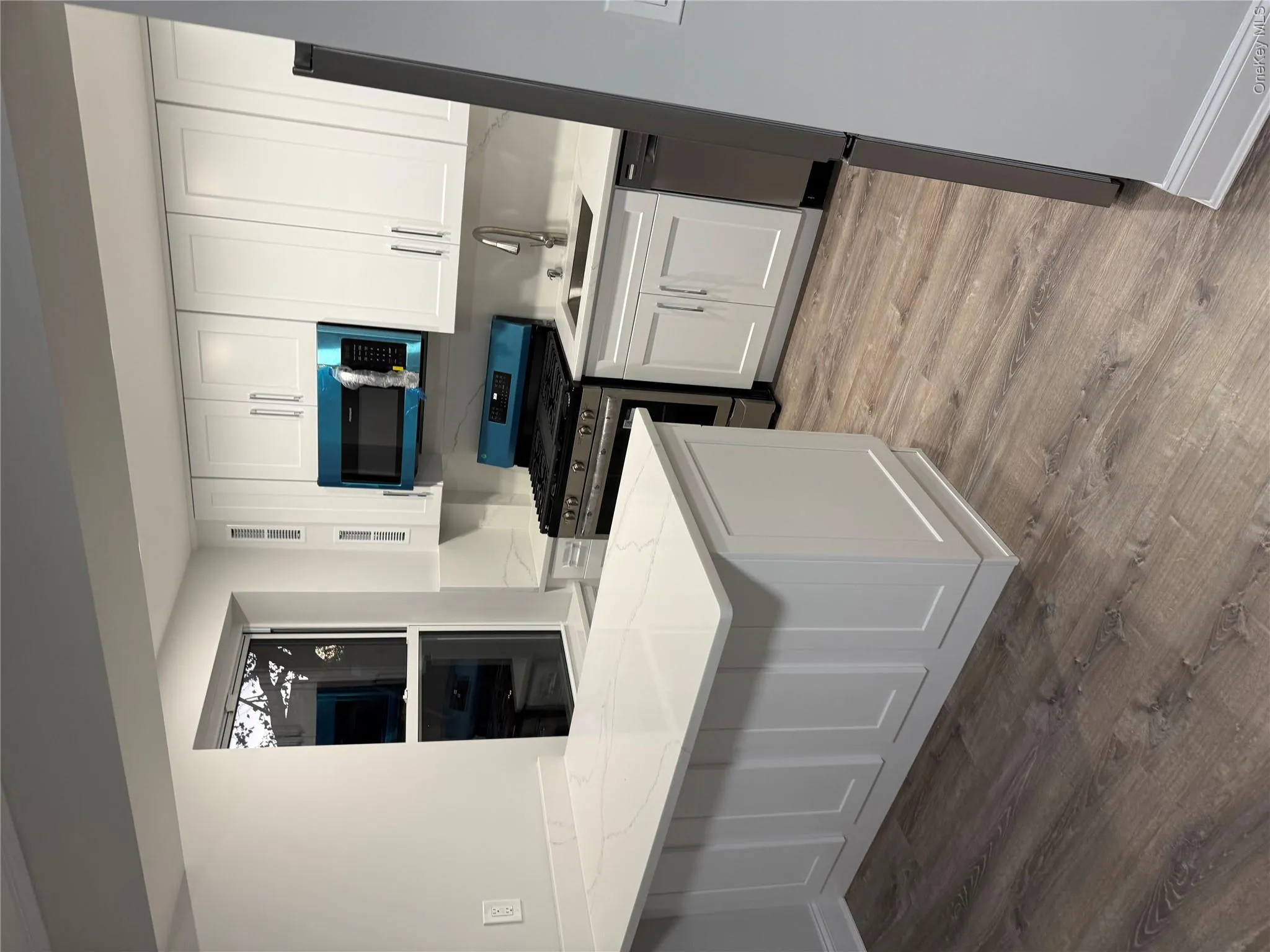 Kitchen featuring white shaker-style cabinetry, white countertops with grey veining, a built-in peninsula, stainless steel appliances, and wood-finish flooring Kitchen featuring white shaker-style cabinetry, white countertops with grey veining, a built-in peninsula, stainless steel appliances, and wood-finish flooring