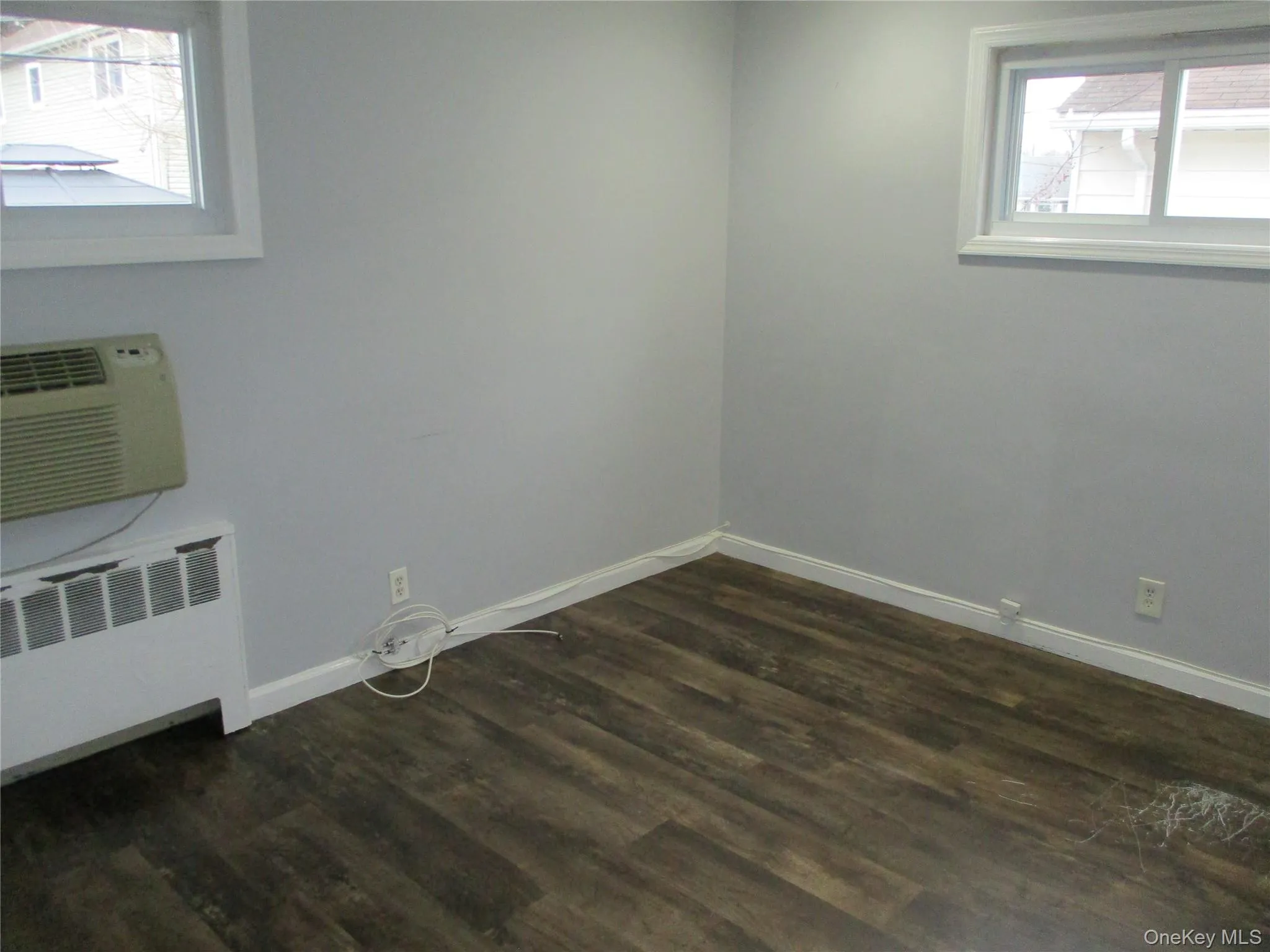 Empty room with radiator heating unit, a wall mounted AC, and dark wood-type flooring Empty room with radiator heating unit, a wall mounted AC, and dark wood-type flooring