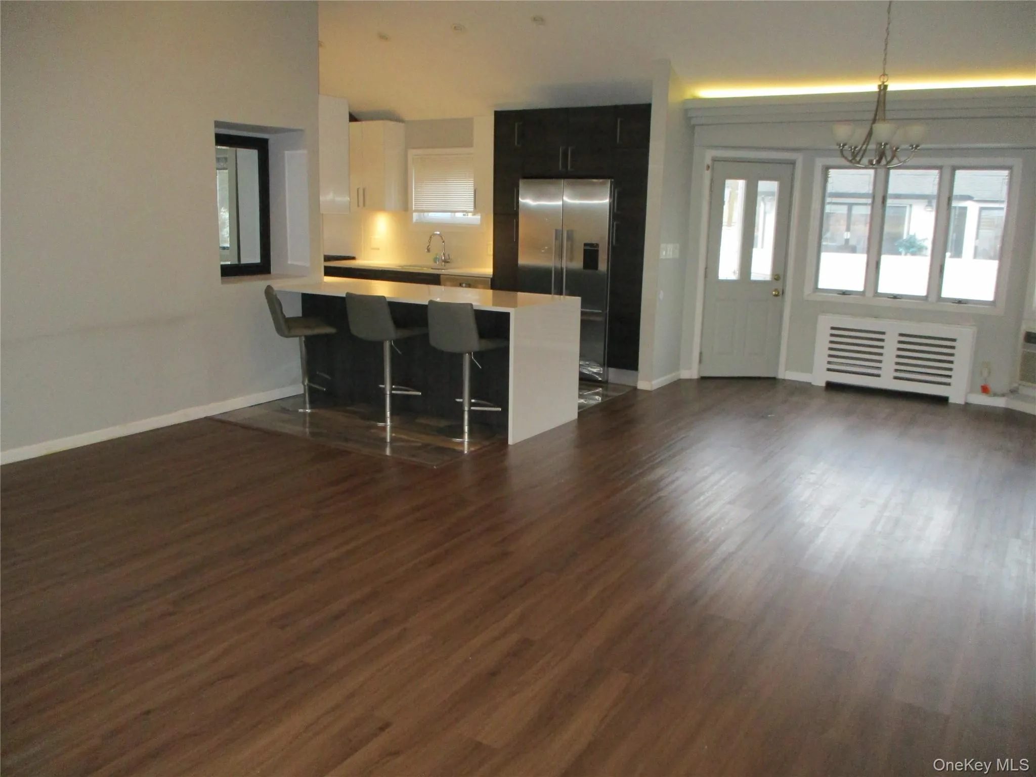 Kitchen featuring radiator heating unit, stainless steel fridge, light countertops, a kitchen bar, and open floor plan Kitchen featuring radiator heating unit, stainless steel fridge, light countertops, a kitchen bar, and open floor plan