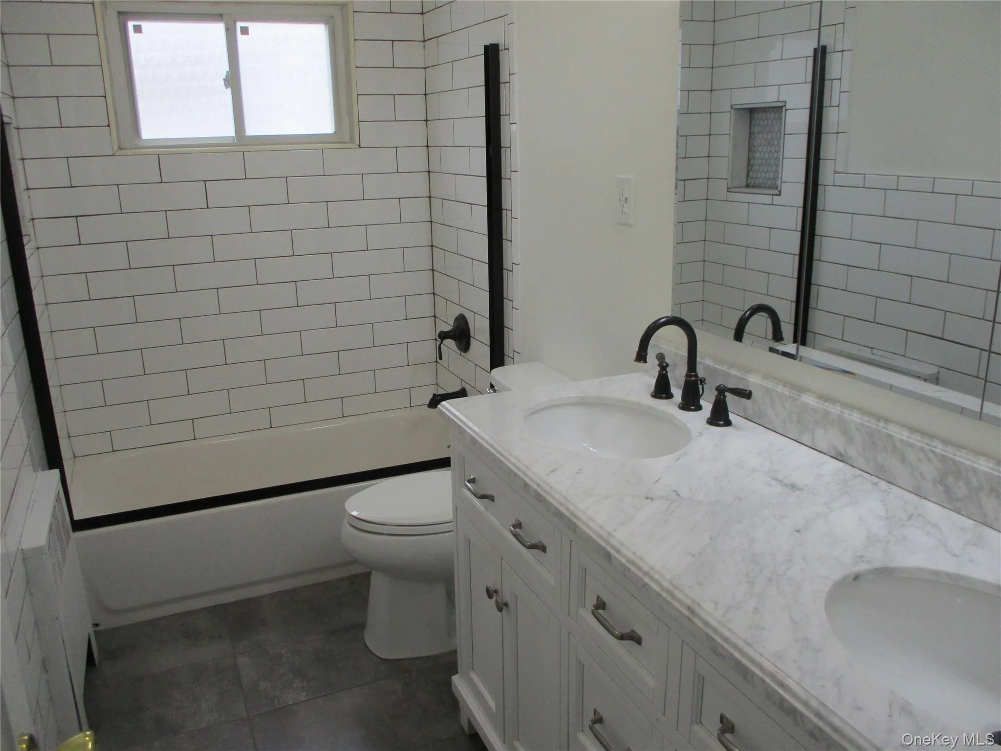 Full bath with double vanity, radiator, shower / tub combination, and dark tile patterned flooring Full bath with double vanity, radiator, shower / tub combination, and dark tile patterned flooring