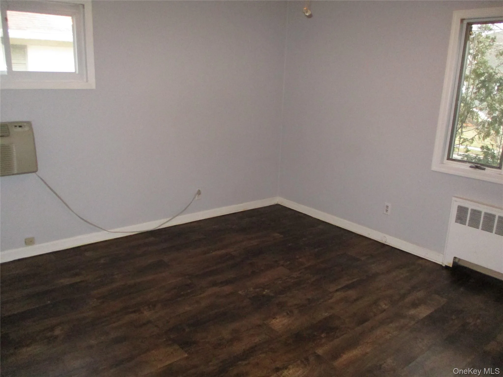 Spare room with dark wood-type flooring, an AC wall unit, and radiator Spare room with dark wood-type flooring, an AC wall unit, and radiator