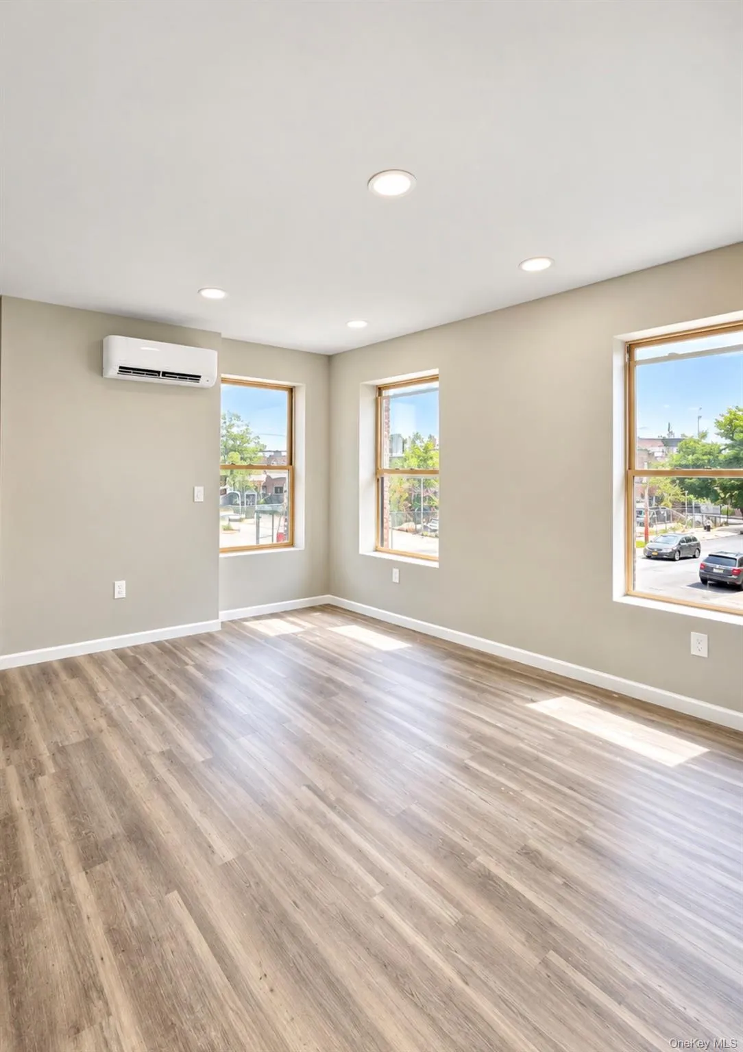 Interior room featuring LVP-finish flooring, recessed lighting, double-hung windows, and a wall-mounted ductless climate control unit Interior room featuring LVP-finish flooring, recessed lighting, double-hung windows, and a wall-mounted ductless climate control unit