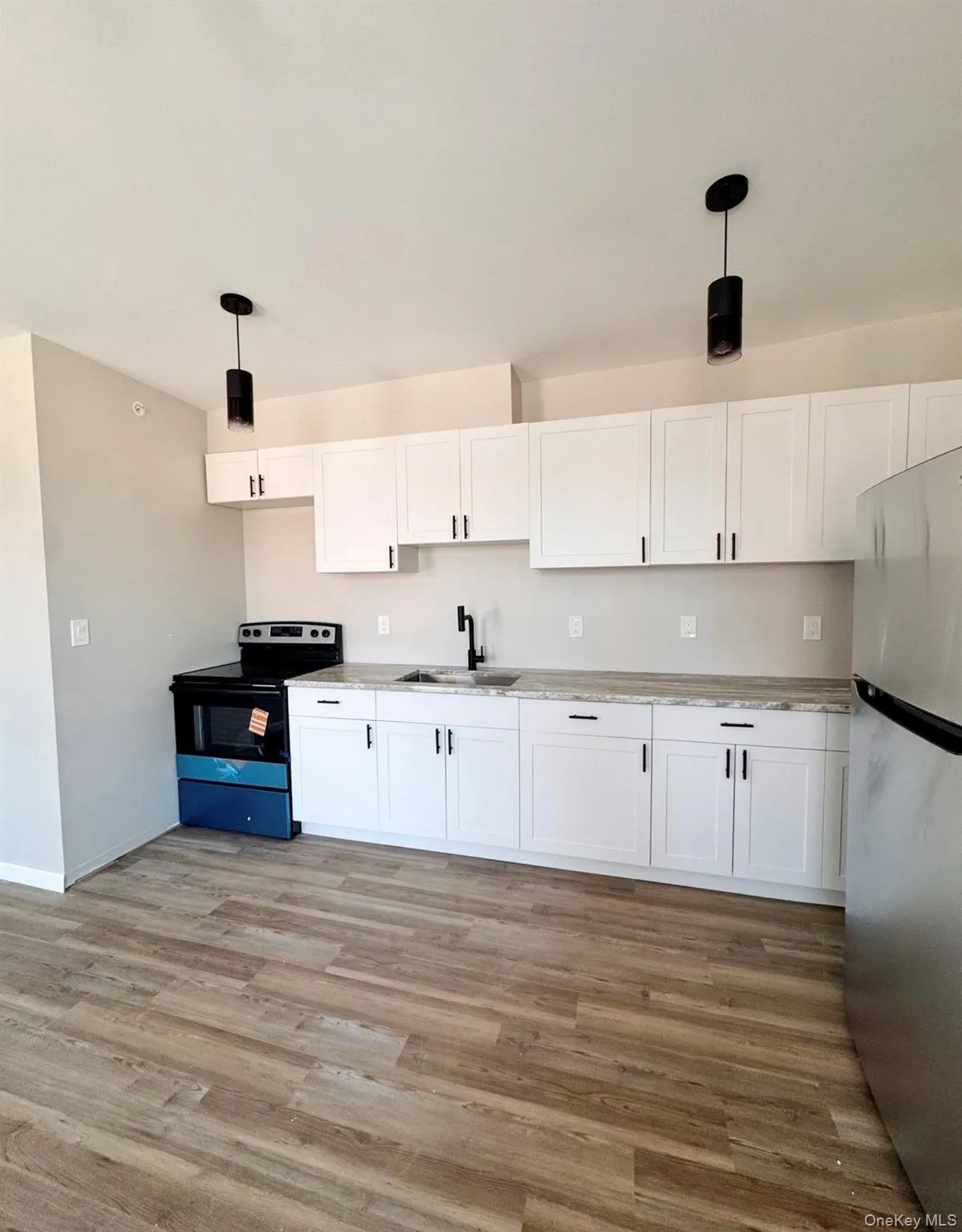 Kitchen featuring white shaker-style cabinetry, stone-patterned countertops, LVP-finish flooring, stainless steel appliances, and matte black pendant lighting Kitchen featuring white shaker-style cabinetry, stone-patterned countertops, LVP-finish flooring, stainless steel appliances, and matte black pendant lighting