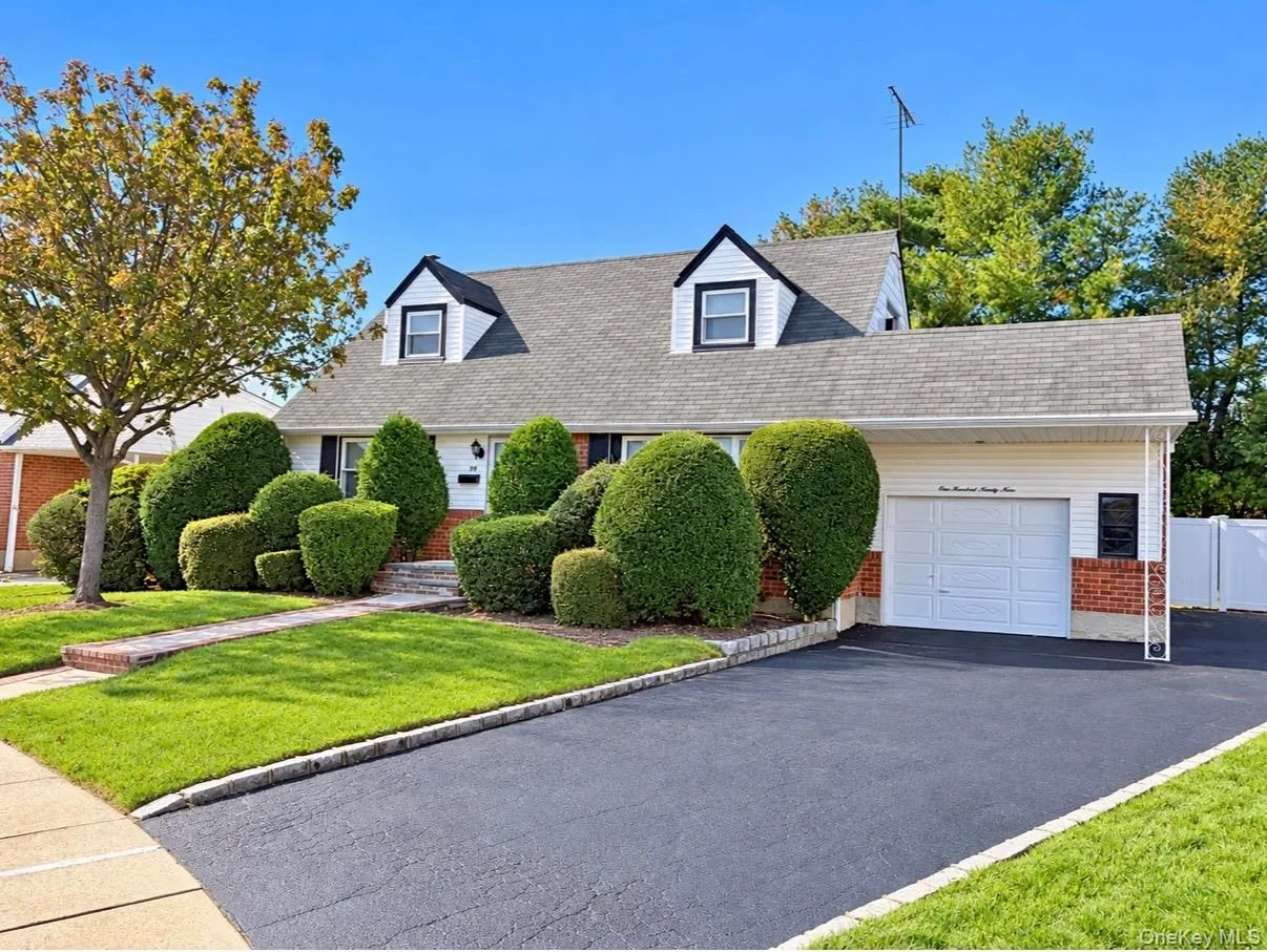 Cape Cod exterior featuring dormer windows brick and siding facade, an attached garage, and a paved driveway Cape Cod exterior featuring dormer windows brick and siding facade, an attached garage, and a paved driveway