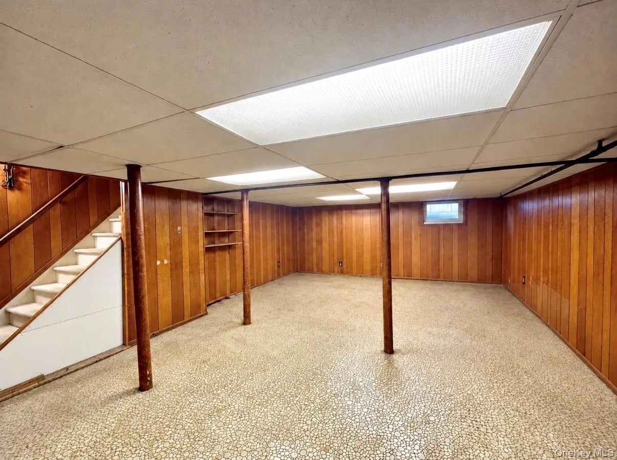 Finished lower level featuring full-height wood-finish paneling, drop ceiling with recessed lighting, integrated shelving, and carpeted stairs with a white banister Finished lower level featuring full-height wood-finish paneling, drop ceiling with recessed lighting, integrated shelving, and carpeted stairs with a white banister