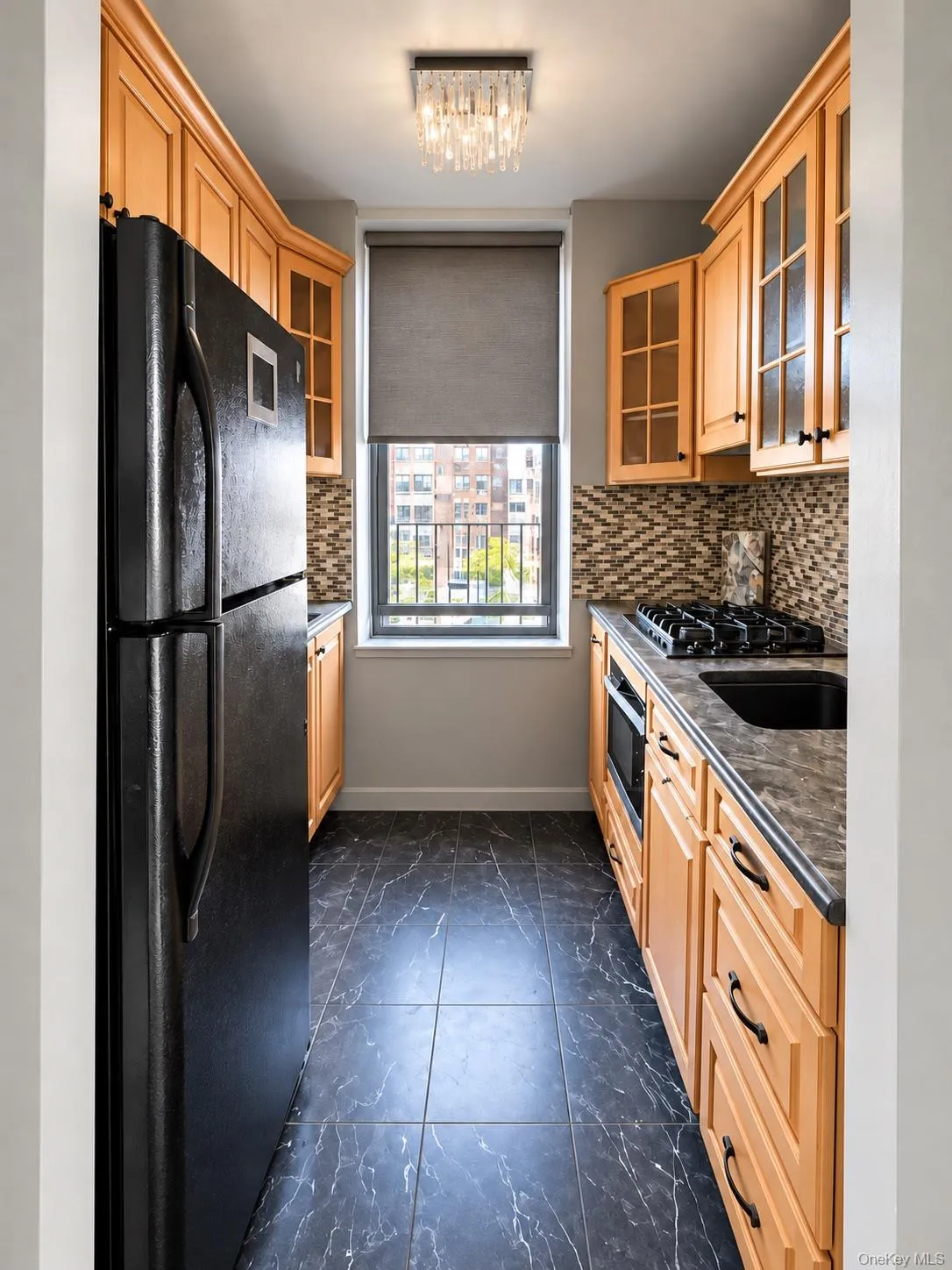 Kitchen featuring wood cabinetry, stone-patterned countertops, mosaic tile backsplash, black stone-patterned tile flooring, and integrated black appliances Kitchen featuring wood cabinetry, stone-patterned countertops, mosaic tile backsplash, black stone-patterned tile flooring, and integrated black appliances
