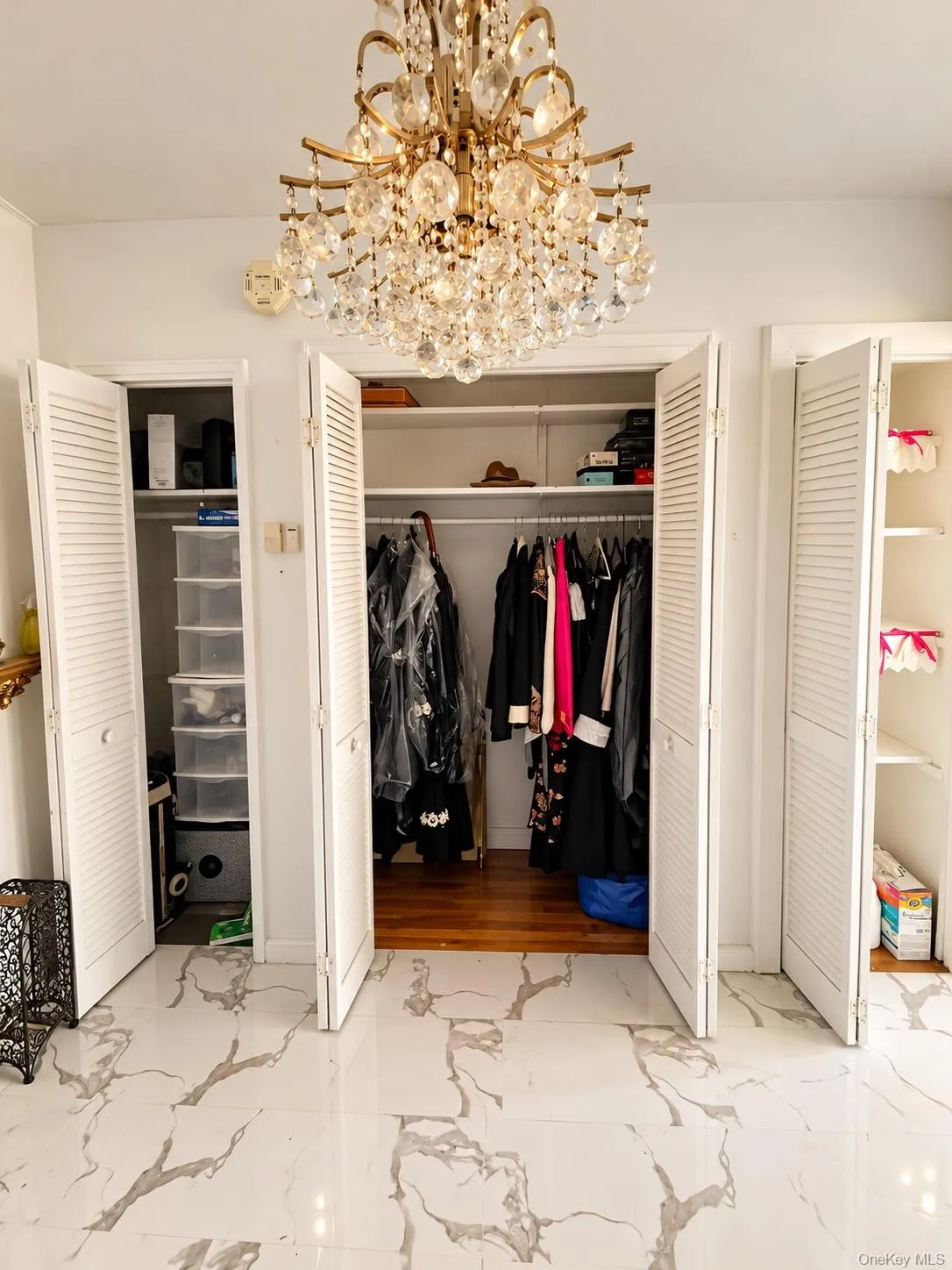 Large crystal chandelier, white louvered closet doors, and polished stone-finish flooring with intricate veining Large crystal chandelier, white louvered closet doors, and polished stone-finish flooring with intricate veining