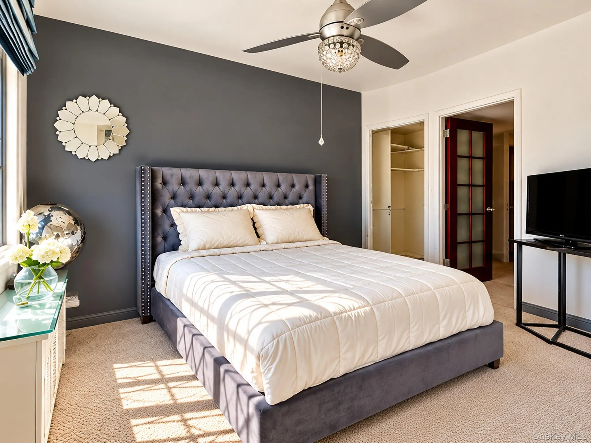 Bedroom featuring a charcoal accent wall, neutral carpeting, ceiling fan with crystal-style light fixture, and a glass-paneled interior door Bedroom featuring a charcoal accent wall, neutral carpeting, ceiling fan with crystal-style light fixture, and a glass-paneled interior door