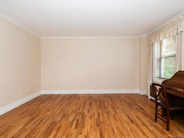 Room featuring wood-finish flooring, crown molding, and a window with integrated radiator cover Room featuring wood-finish flooring, crown molding, and a window with integrated radiator cover