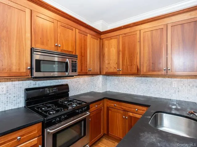 Custom wood cabinetry, stainless steel microwave, black gas range, dark countertops, and mosaic tile backsplash Custom wood cabinetry, stainless steel microwave, black gas range, dark countertops, and mosaic tile backsplash