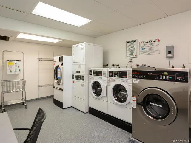 Common laundry facility featuring commercial-grade front-loading washing machines, a stacked dryer unit, and drop-ceiling with recessed fluorescent lighting Common laundry facility featuring commercial-grade front-loading washing machines, a stacked dryer unit, and drop-ceiling with recessed fluorescent lighting