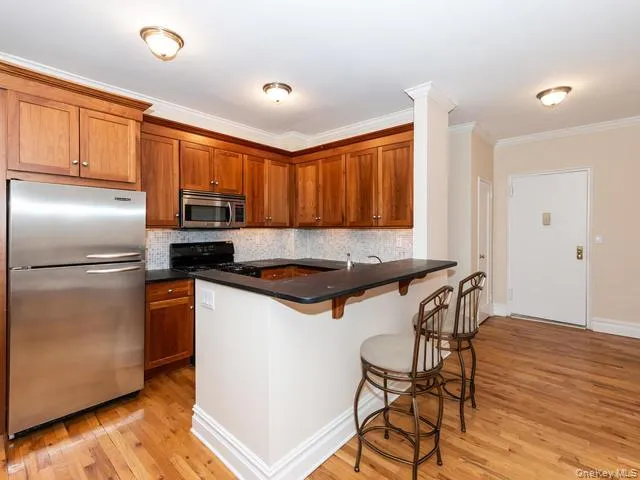 Kitchen featuring custom wood cabinetry, granite countertops, stainless steel refrigerator and built-in microwave, wood-finish flooring, and a breakfast bar Kitchen featuring custom wood cabinetry, granite countertops, stainless steel refrigerator and built-in microwave, wood-finish flooring, and a breakfast bar