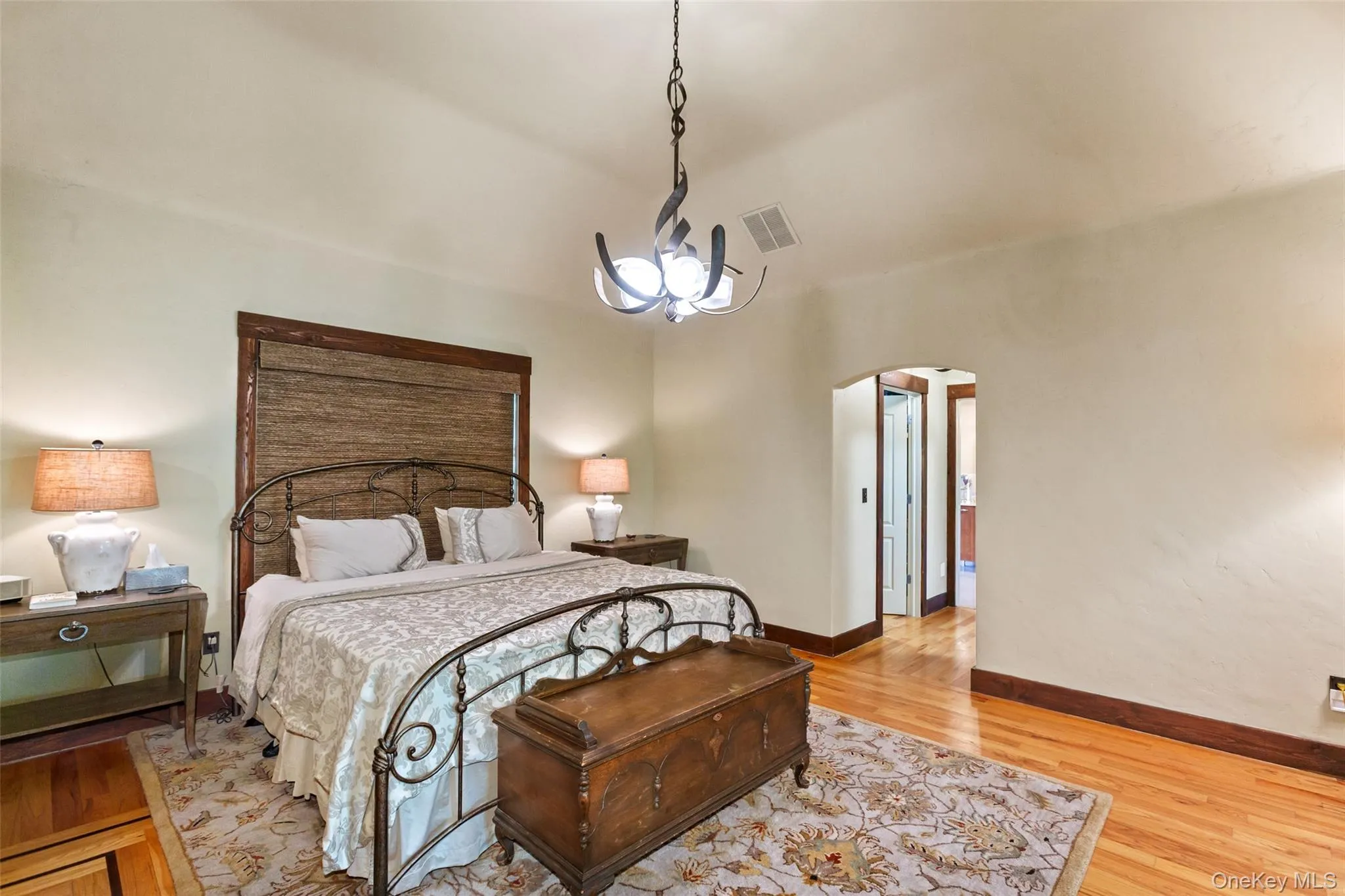 Bedroom featuring arched walkways, light wood-style floors, baseboards, high vaulted ceiling, and a chandelier Bedroom featuring arched walkways, light wood-style floors, baseboards, high vaulted ceiling, and a chandelier