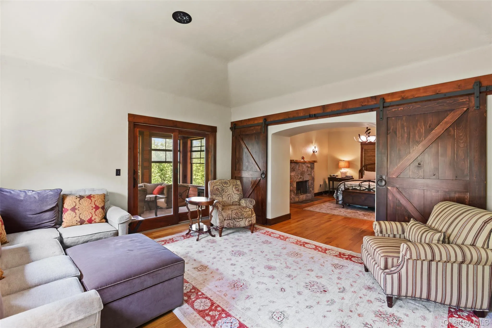 Living room with a barn door, wood finished floors, arched walkways, and high vaulted ceiling Living room with a barn door, wood finished floors, arched walkways, and high vaulted ceiling