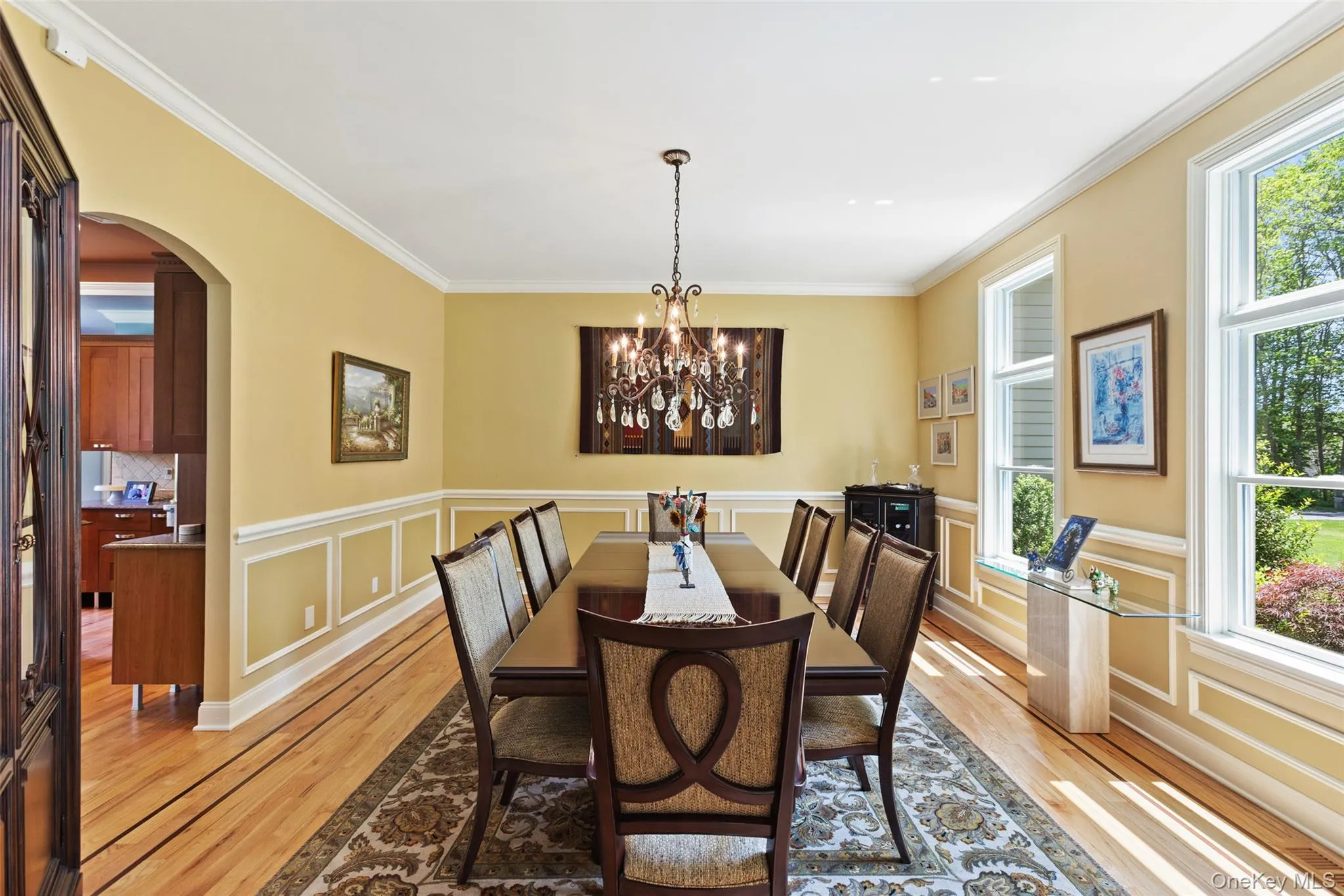 Dining space with light wood finished floors, arched walkways, crown molding, a chandelier, and a decorative wall Dining space with light wood finished floors, arched walkways, crown molding, a chandelier, and a decorative wall