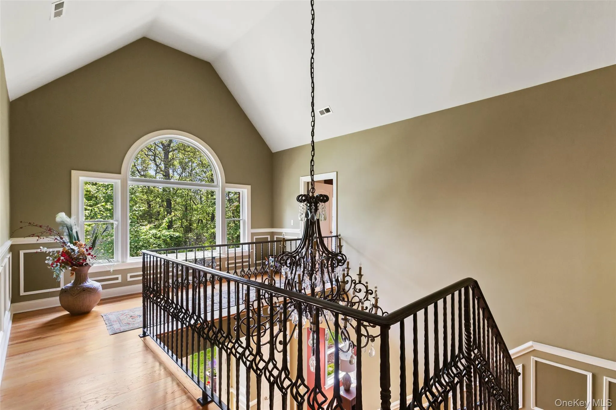Stairs with high vaulted ceiling, a chandelier, wood finished floors, and a wainscoted wall Stairs with high vaulted ceiling, a chandelier, wood finished floors, and a wainscoted wall