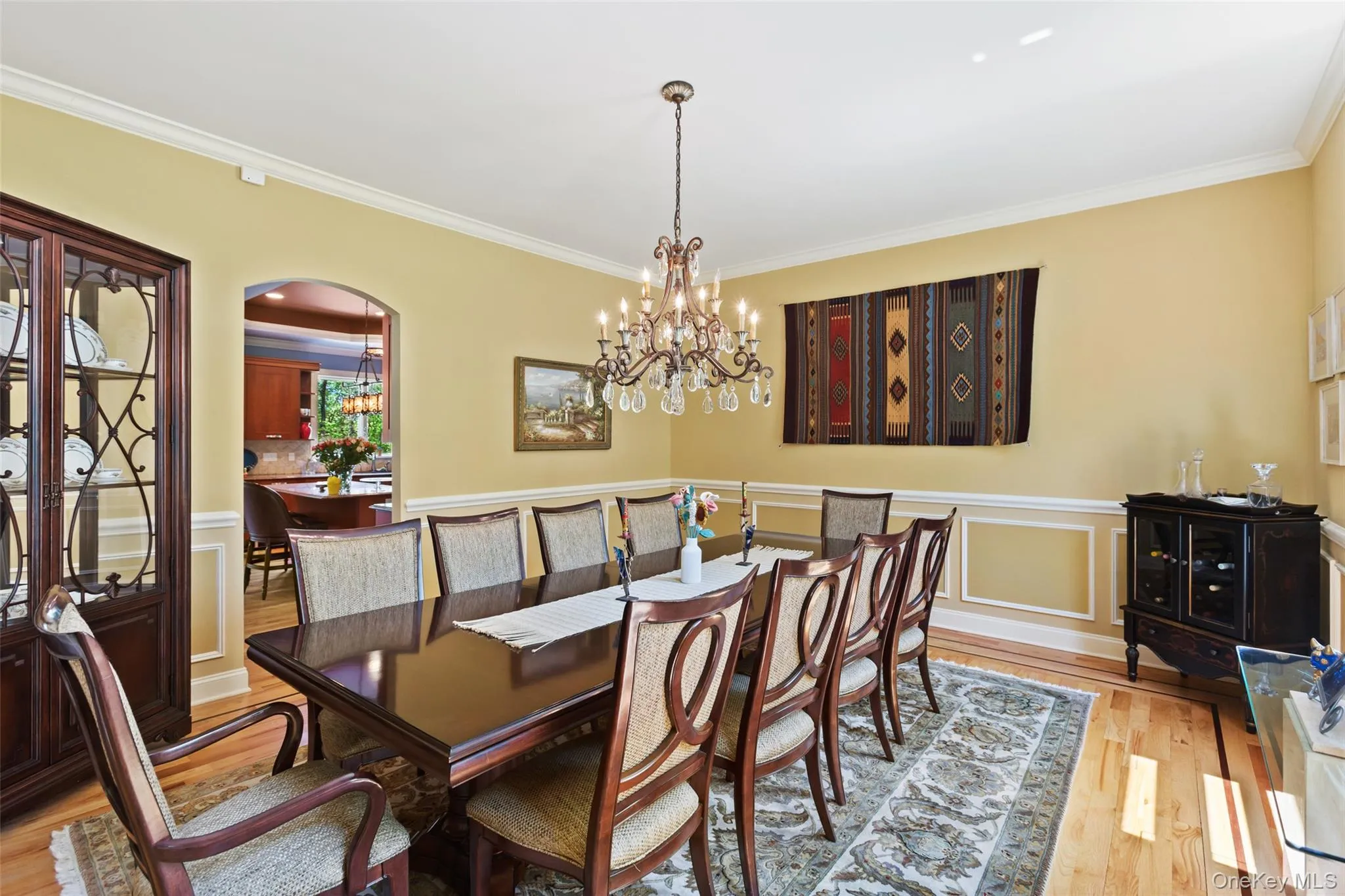 Dining space featuring arched walkways, crown molding, wood finished floors, a chandelier, and a wainscoted wall Dining space featuring arched walkways, crown molding, wood finished floors, a chandelier, and a wainscoted wall