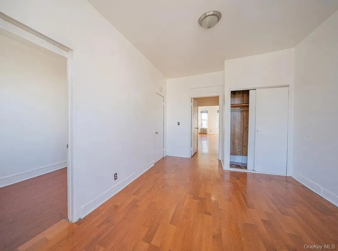 Interior room featuring wood-finish flooring, white walls, flush-mount ceiling lighting, and a reach-in closet with sliding doors. Interior room featuring wood-finish flooring, white walls, flush-mount ceiling lighting, and a reach-in closet with sliding doors.