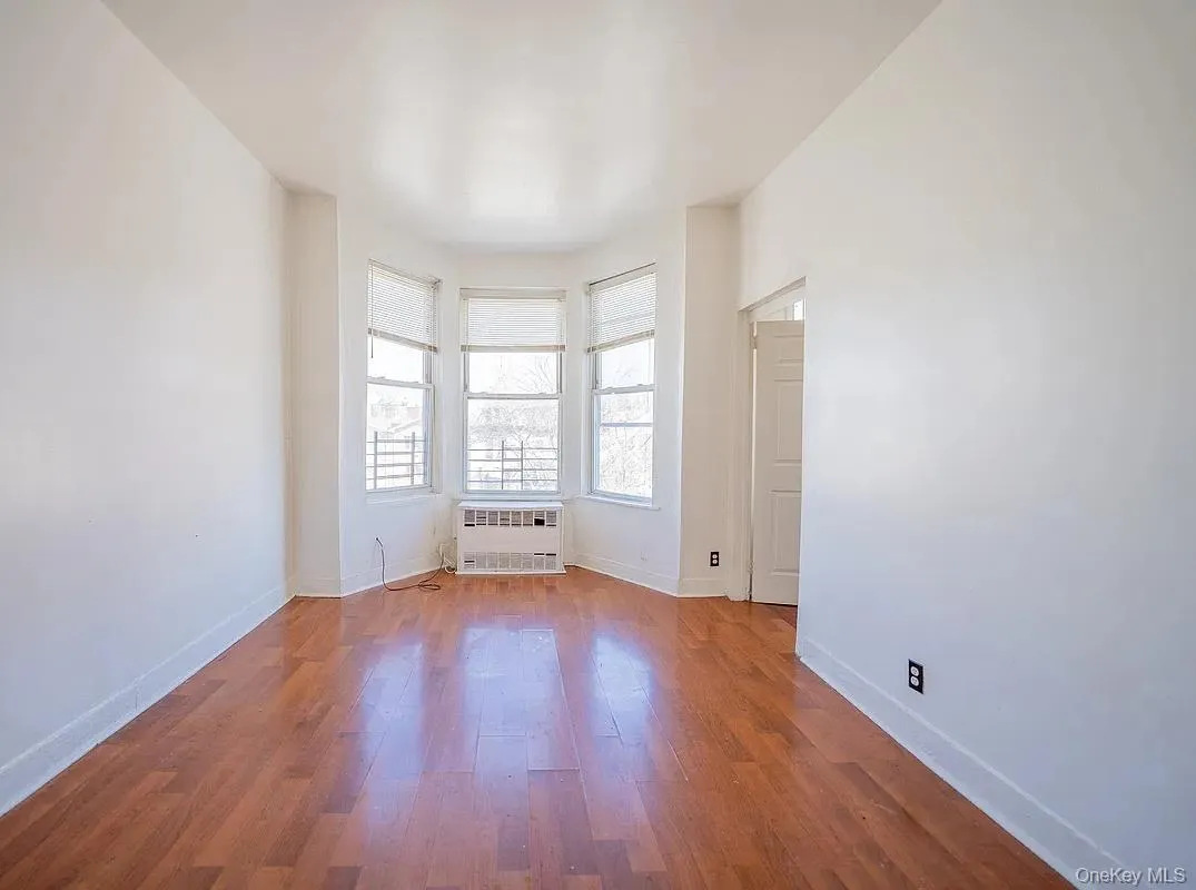 Interior space featuring wood-finish flooring, a three-panel bay window configuration, and a built-in heating unit. Interior space featuring wood-finish flooring, a three-panel bay window configuration, and a built-in heating unit.