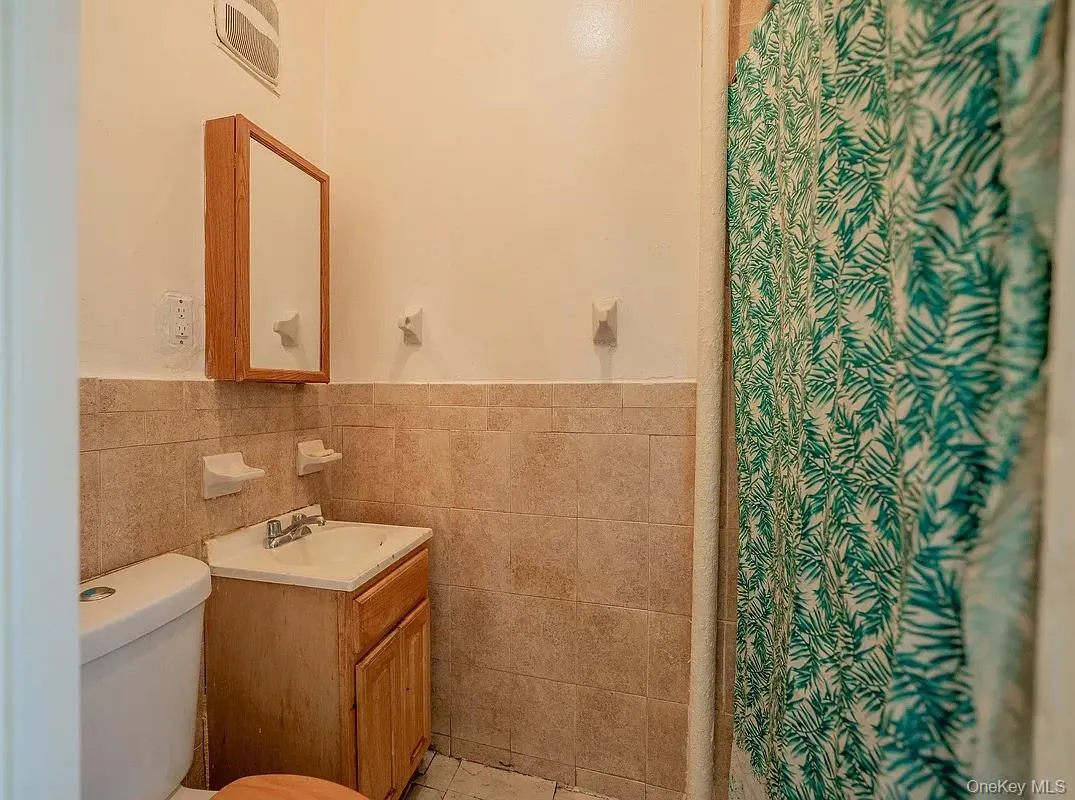 Bathroom featuring a wood-finish vanity with a drop-in sink, wall-mounted medicine cabinet, and tiled wall surround Bathroom featuring a wood-finish vanity with a drop-in sink, wall-mounted medicine cabinet, and tiled wall surround