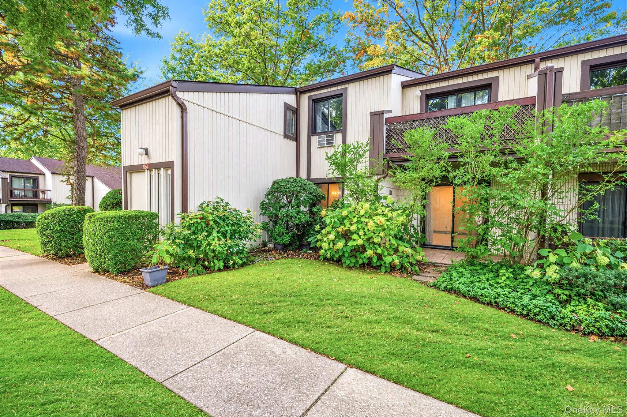 Multi-level exterior featuring vertical siding, a second-story wooden balcony, and established landscape shrubbery Multi-level exterior featuring vertical siding, a second-story wooden balcony, and established landscape shrubbery