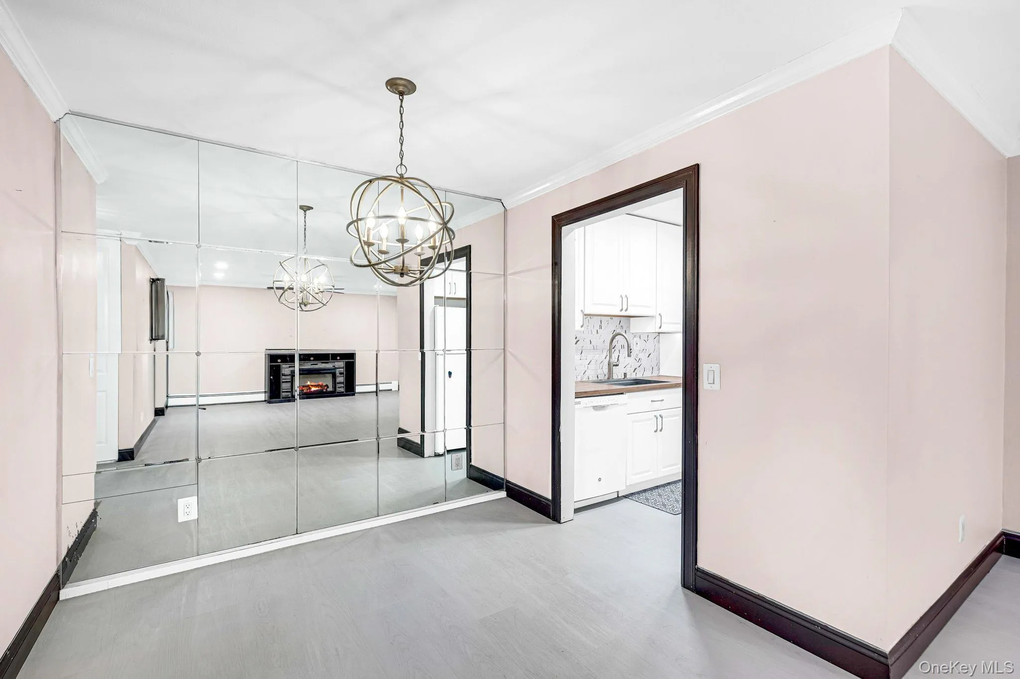Floor-to-ceiling wall mirror, crown molding, spherical metal chandelier, and wood-finish flooring Floor-to-ceiling wall mirror, crown molding, spherical metal chandelier, and wood-finish flooring