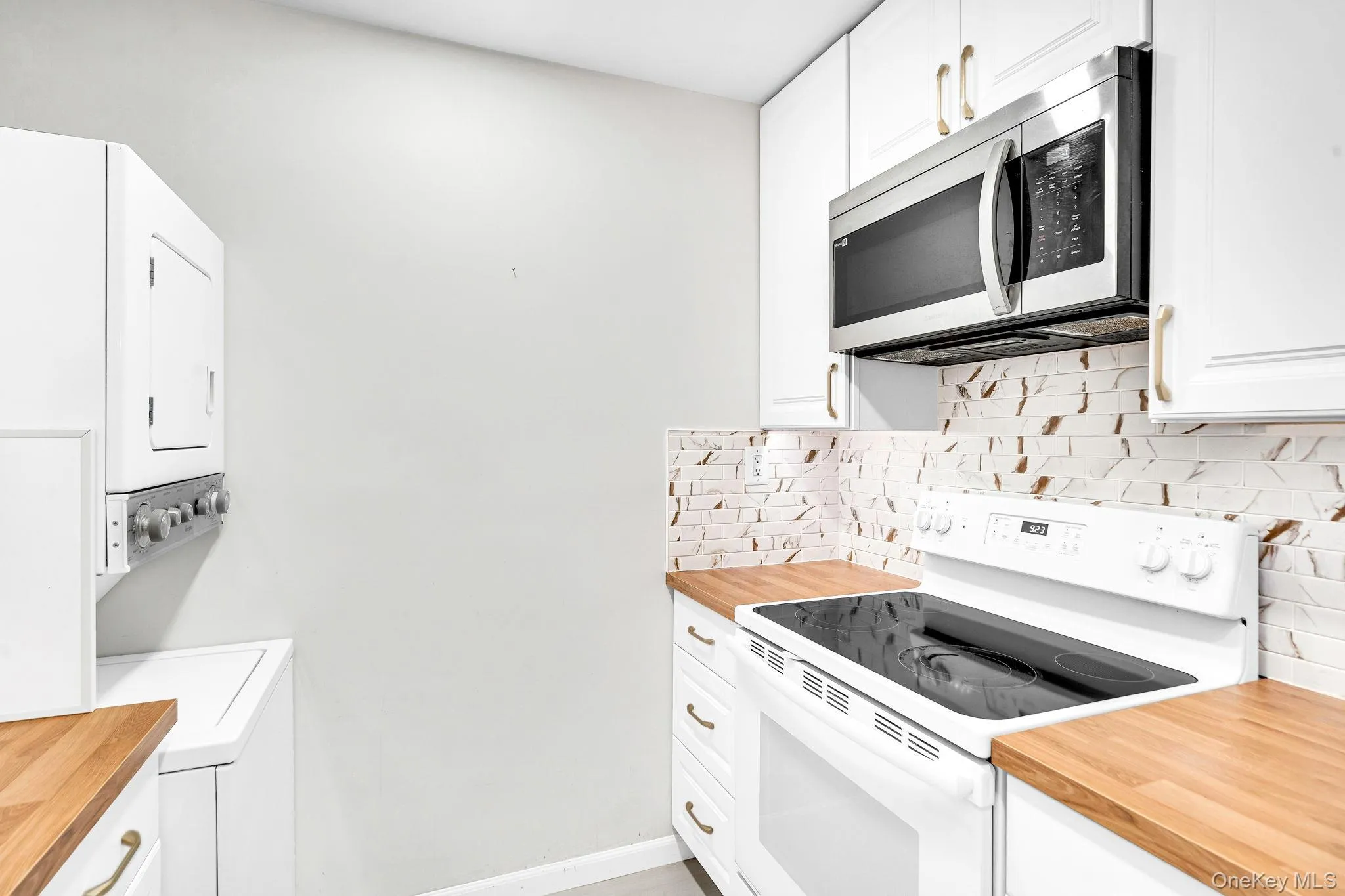 Kitchen featuring white cabinetry, butcher block countertops, stainless steel microwave, white electric range, and patterned tile backsplash Kitchen featuring white cabinetry, butcher block countertops, stainless steel microwave, white electric range, and patterned tile backsplash