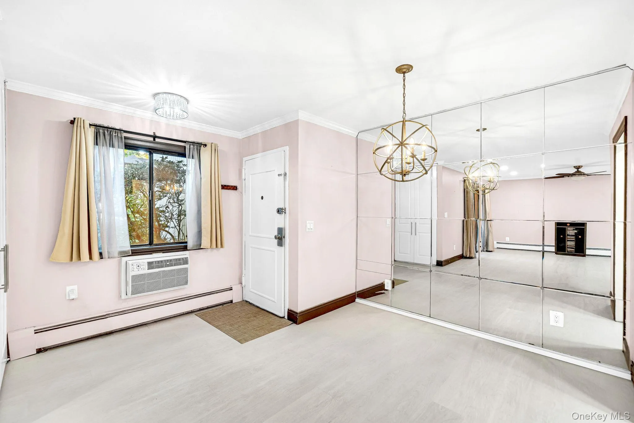 Floor-to-ceiling wall mirror, crown molding, spherical metal chandelier, and wood-finish flooring Floor-to-ceiling wall mirror, crown molding, spherical metal chandelier, and wood-finish flooring