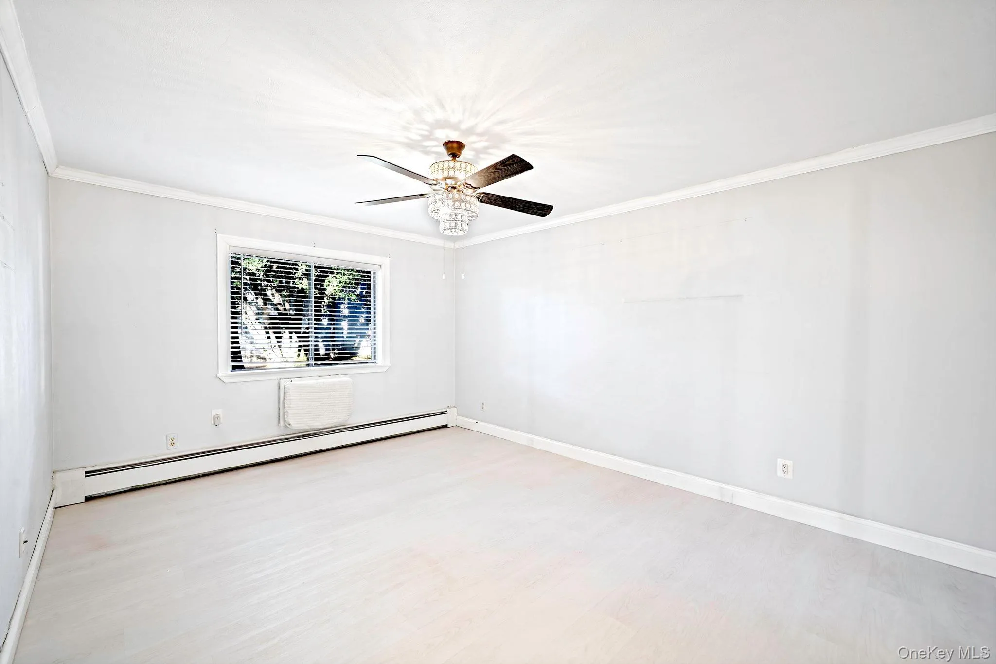Interior room featuring neutral-toned walls, wood-finish flooring, a multi-blade ceiling fan with integrated crystal-style light fixture, and crown molding Interior room featuring neutral-toned walls, wood-finish flooring, a multi-blade ceiling fan with integrated crystal-style light fixture, and crown molding