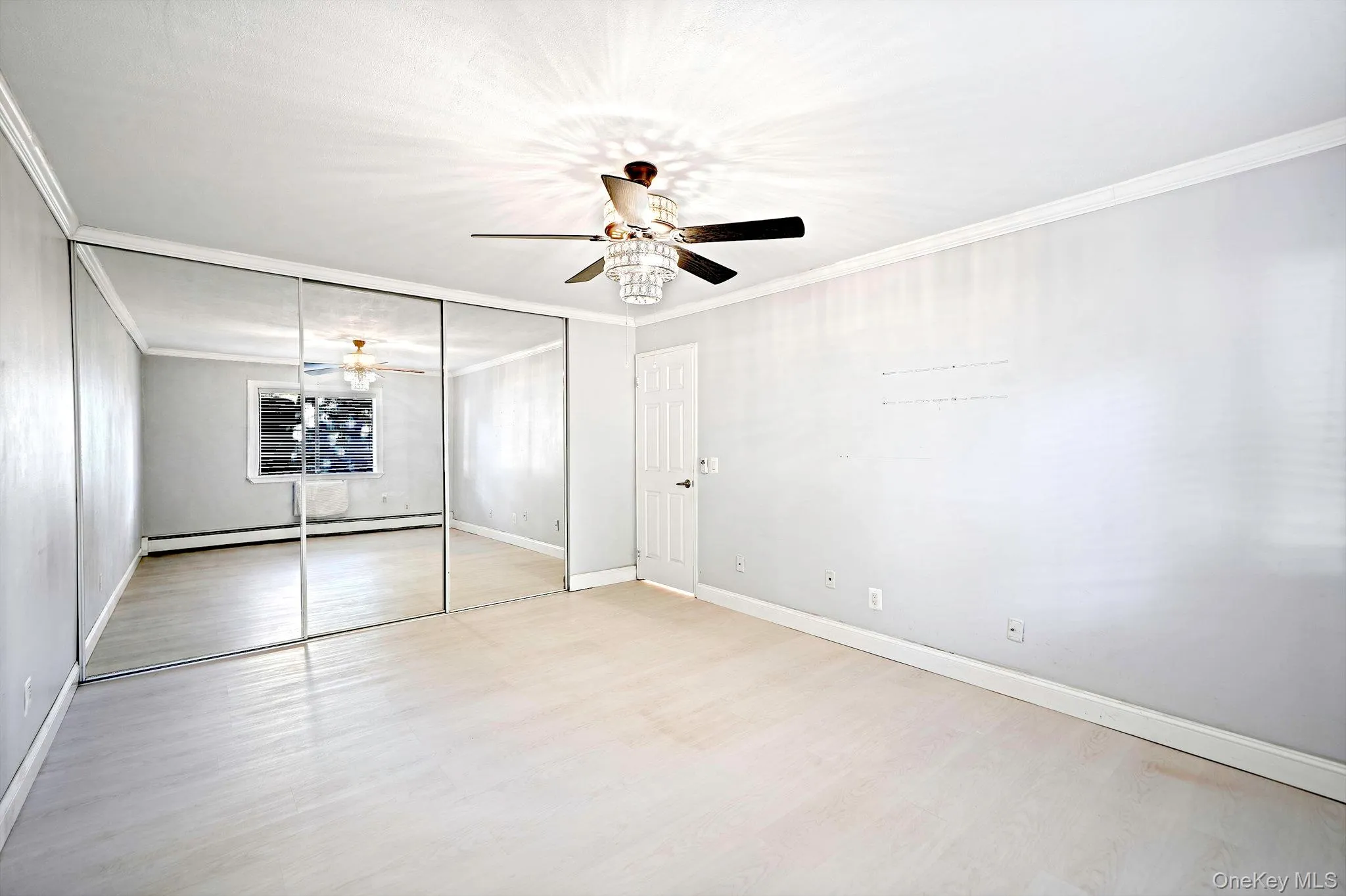 Second view of Primary Bedroom - Room featuring wood-finish flooring, floor-to-ceiling mirrored closet doors, a crystal-accented ceiling fan with integrated lighting, and crown molding Second view of Primary Bedroom - Room featuring wood-finish flooring, floor-to-ceiling mirrored closet doors, a crystal-accented ceiling fan with integrated lighting, and crown molding