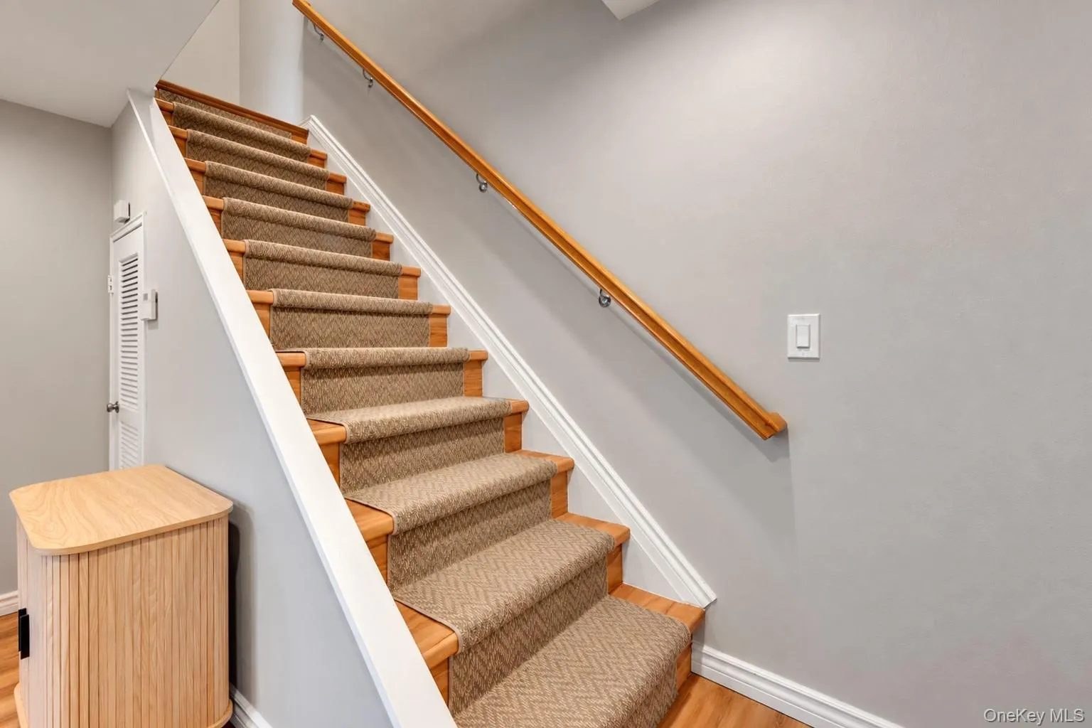 Staircase featuring wood-finish treads, a patterned carpet runner, and a natural wood-finish handrail Staircase featuring wood-finish treads, a patterned carpet runner, and a natural wood-finish handrail