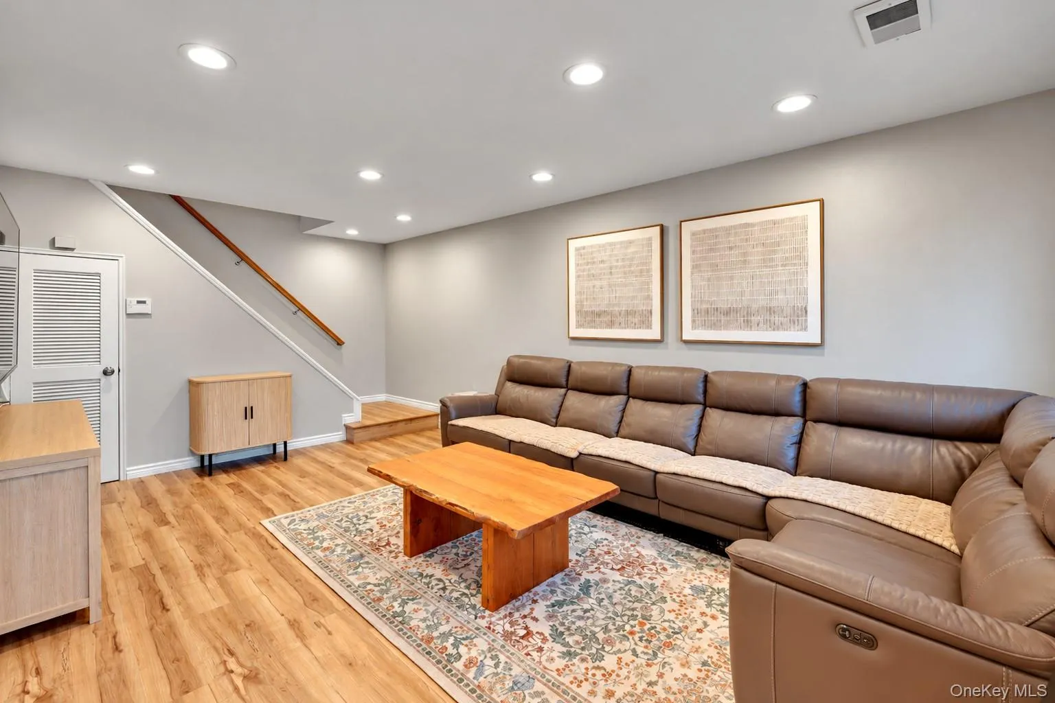 Neutral-toned interior space featuring wood-finish flooring, recessed lighting, and a staircase with a wooden handrail Neutral-toned interior space featuring wood-finish flooring, recessed lighting, and a staircase with a wooden handrail