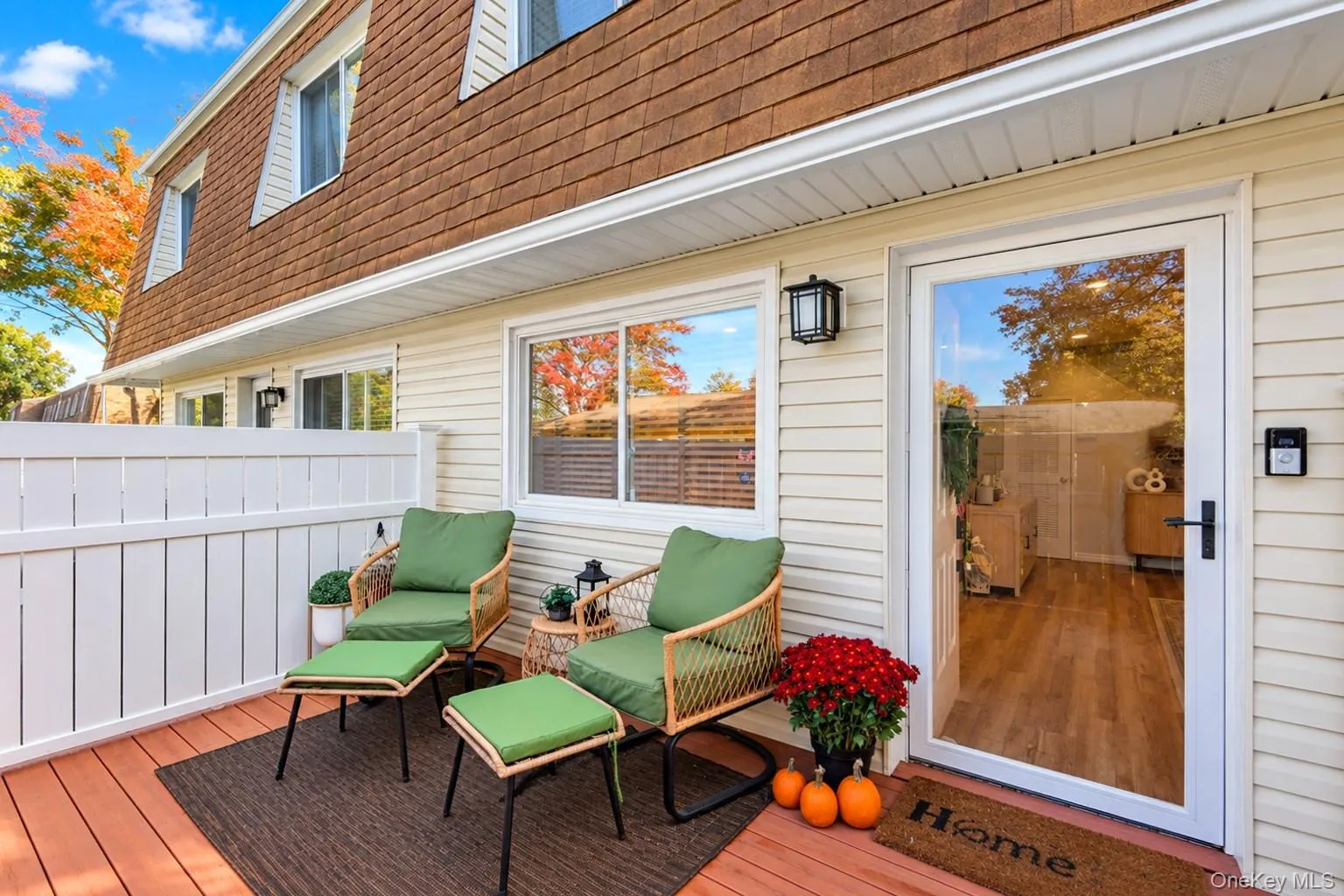 Exterior patio featuring wood-finish decking, white vinyl privacy fencing, horizontal siding, and a full-light glass entry door with matte black hardware Exterior patio featuring wood-finish decking, white vinyl privacy fencing, horizontal siding, and a full-light glass entry door with matte black hardware