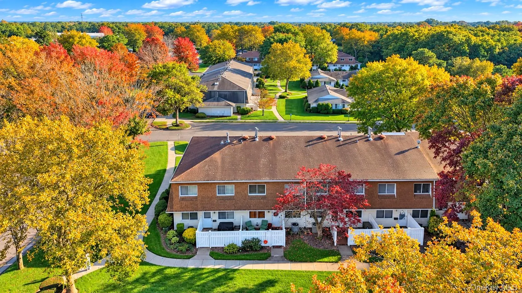 Multi-unit building featuring a shingled roof, brown siding, white privacy fencing, and concrete walkways Multi-unit building featuring a shingled roof, brown siding, white privacy fencing, and concrete walkways