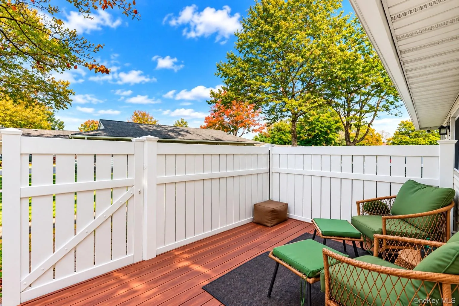 Private patio featuring wood-finish decking, a white vinyl privacy fence, and an integrated gate Private patio featuring wood-finish decking, a white vinyl privacy fence, and an integrated gate