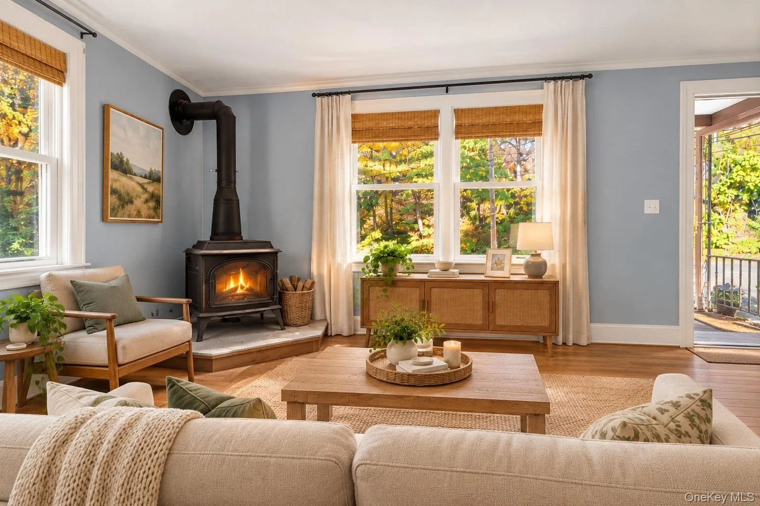 Living area featuring wood-finish flooring, a cast-iron wood stove on a raised stone hearth, and oversized windows with natural light Living area featuring wood-finish flooring, a cast-iron wood stove on a raised stone hearth, and oversized windows with natural light