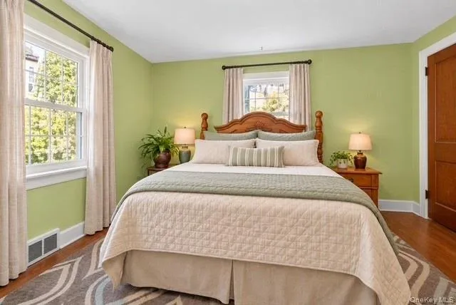 Bedroom interior featuring wood-finish flooring, two double-hung windows, and a solid wood door Bedroom interior featuring wood-finish flooring, two double-hung windows, and a solid wood door