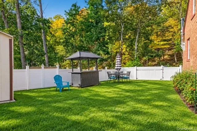 Rear exterior featuring a manicured lawn, white vinyl fencing, a brick structure, and mature trees Rear exterior featuring a manicured lawn, white vinyl fencing, a brick structure, and mature trees