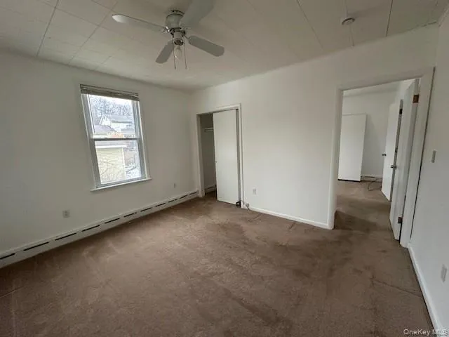 Unfurnished bedroom with baseboard heating, carpet, a ceiling fan, and a closet Unfurnished bedroom with baseboard heating, carpet, a ceiling fan, and a closet